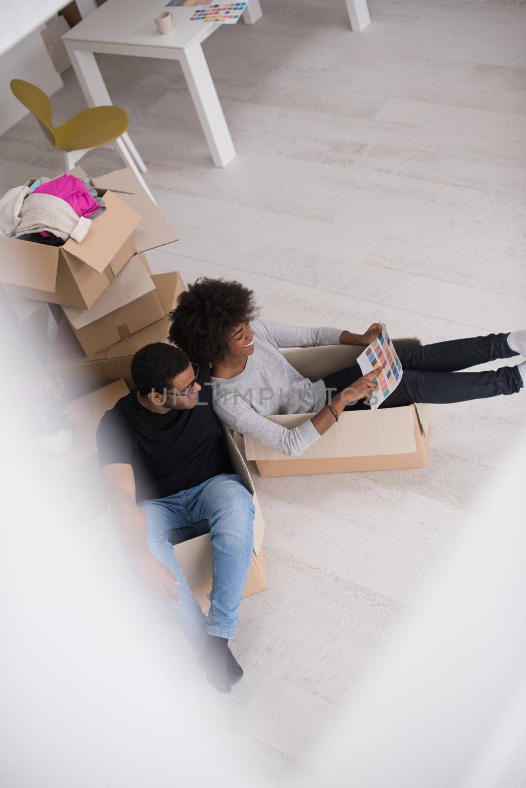 African American couple sitting in a box playing with packing material, having fun after moving in new home