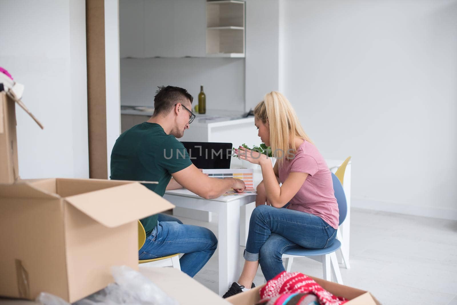 Young couple moving in a new home. Man and woman at the table using notebook laptop computer and plans with boxes around them