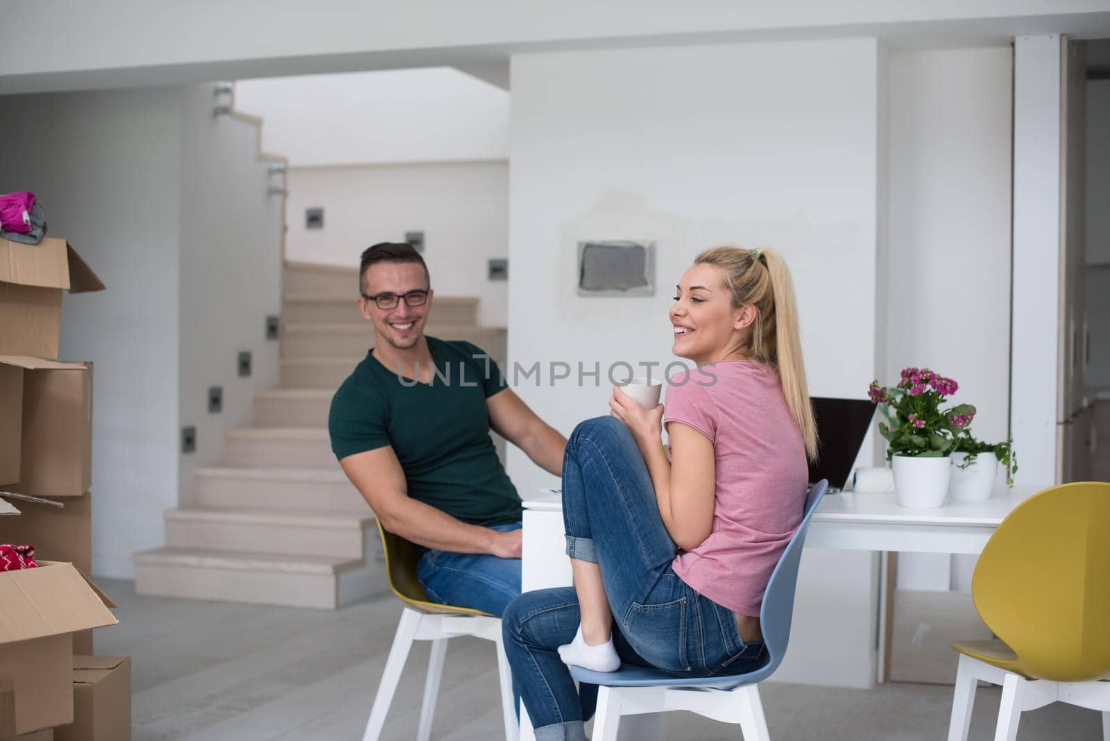 Young couple moving in a new home. Man and woman at the table using notebook laptop computer and plans with boxes around them