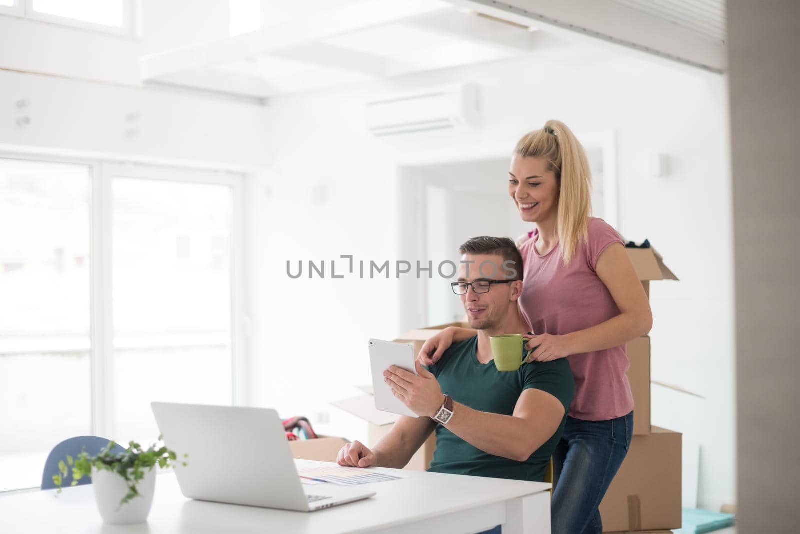 Young couple moving in a new home. Man and woman at the table using notebook laptop computer and plans with boxes around them