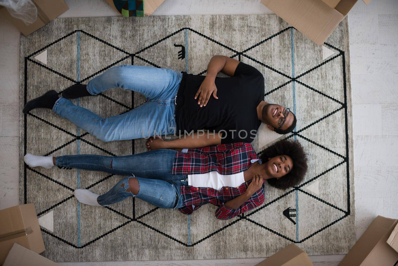 Top view of attractive young African American couple moving, holding hands, looking at camera and smiling while lying among cardboard boxes