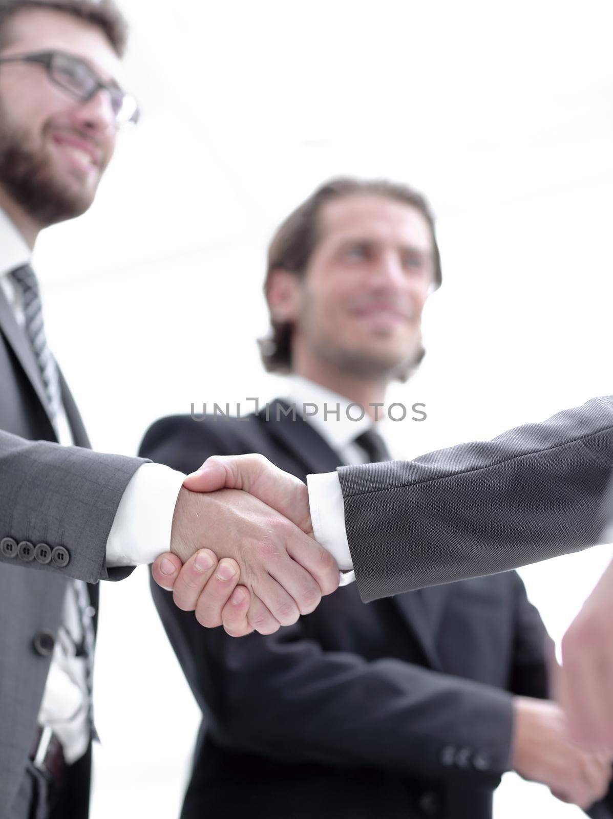 confident businessmen shaking hands and smiling while standing at office together
