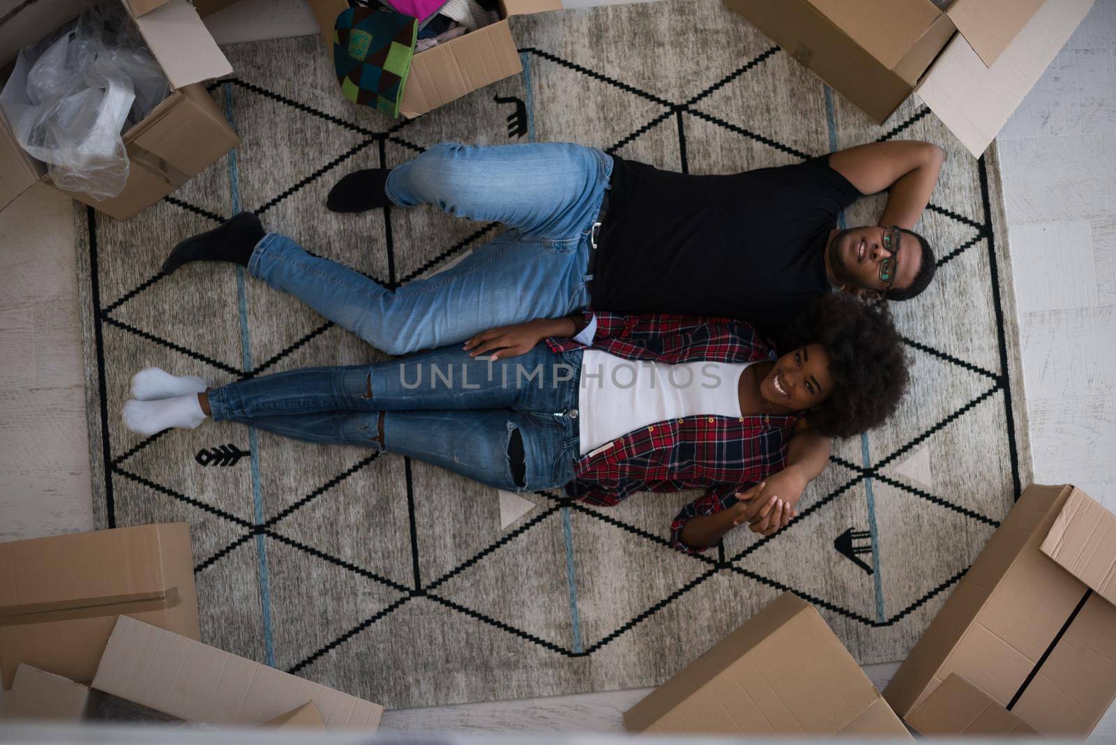 Top view of attractive young African American couple moving, holding hands, looking at camera and smiling while lying among cardboard boxes