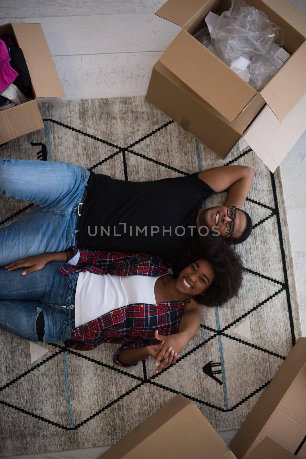 Top view of attractive young African American couple moving, holding hands, looking at camera and smiling while lying among cardboard boxes