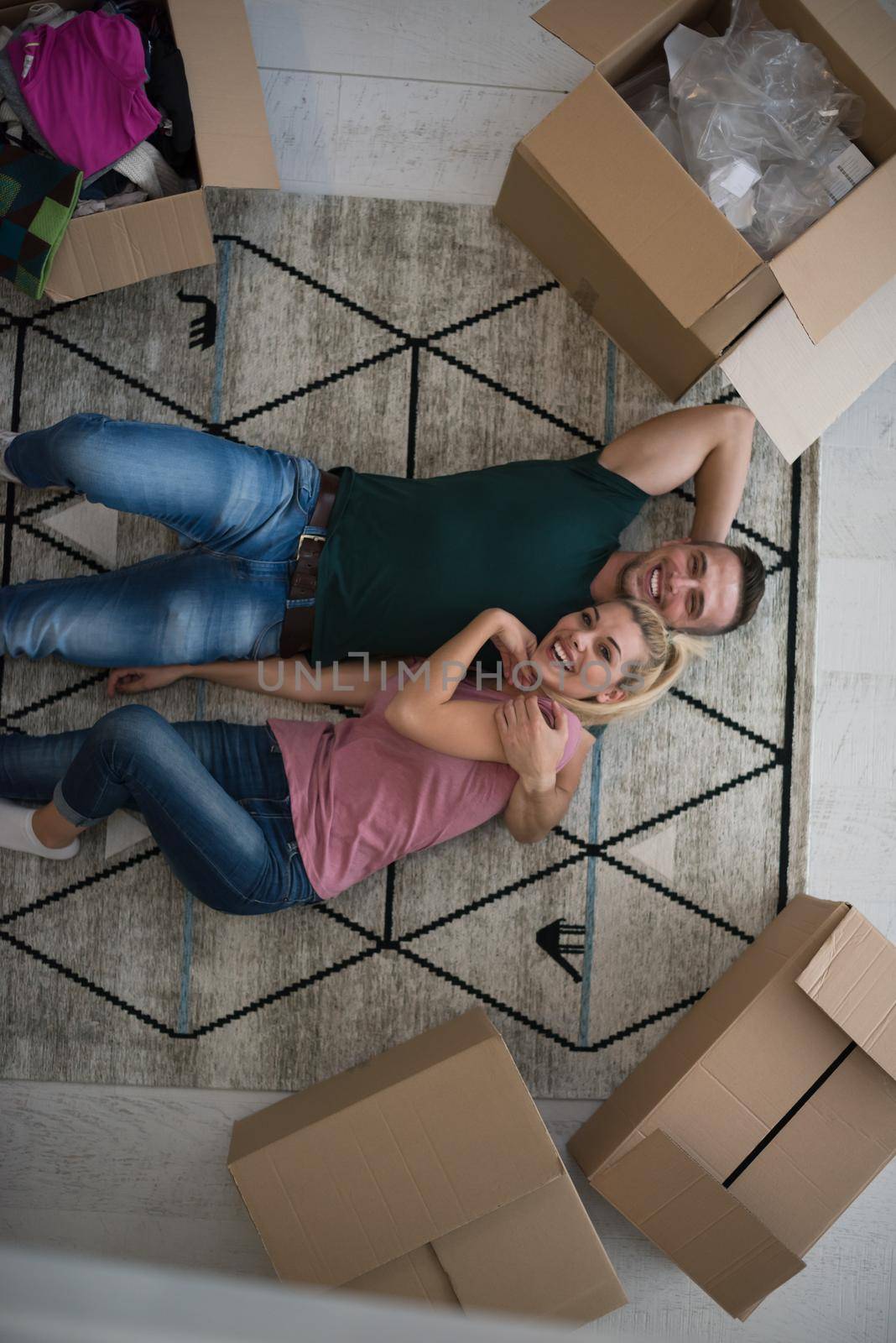 Top view of attractive young couple moving, holding hands, looking at camera and smiling while lying among cardboard boxes