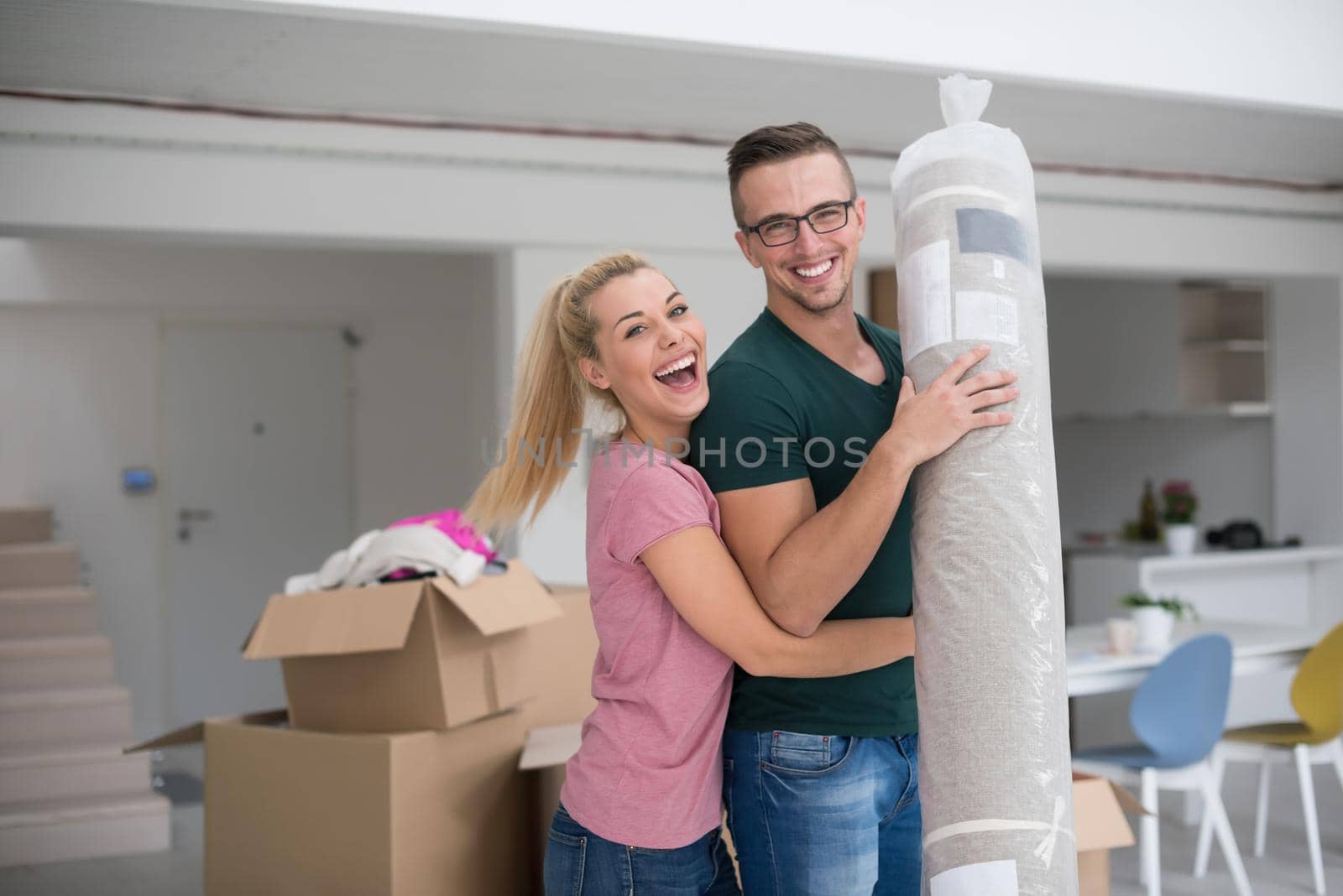 Young couple carrying a carpet moving in to new home together. Home, people, moving and real estate concept