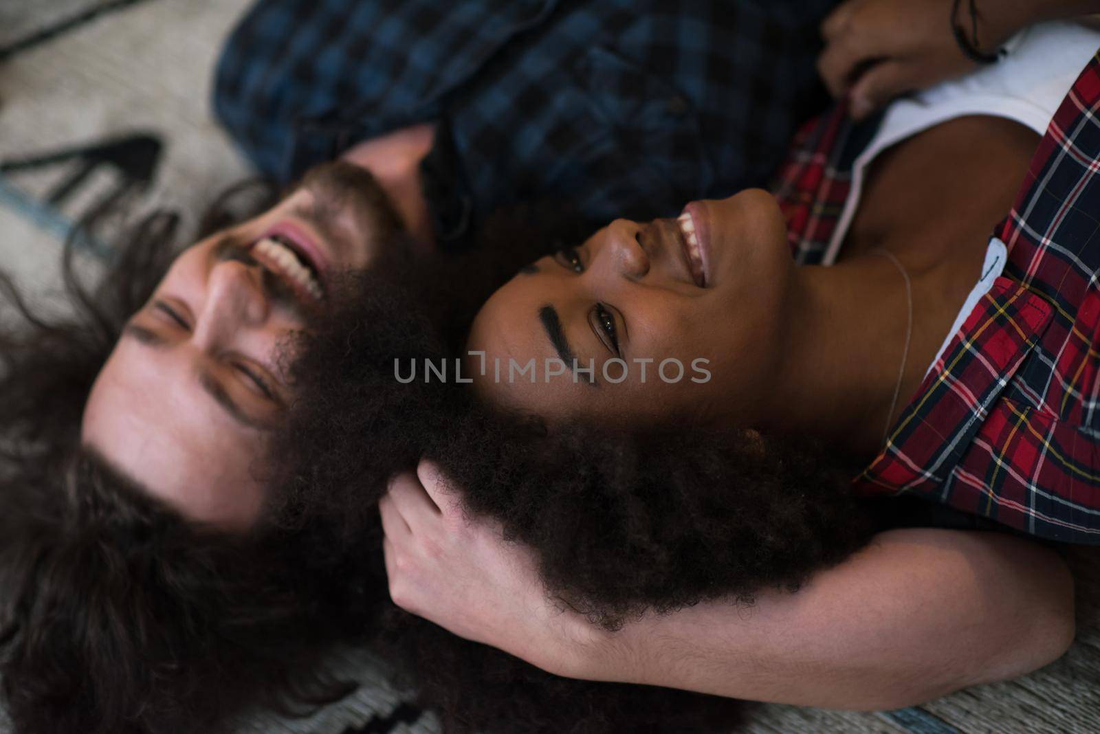 Top view of attractive young multiethnic couple moving, holding hands, looking at camera and smiling while lying among cardboard boxes