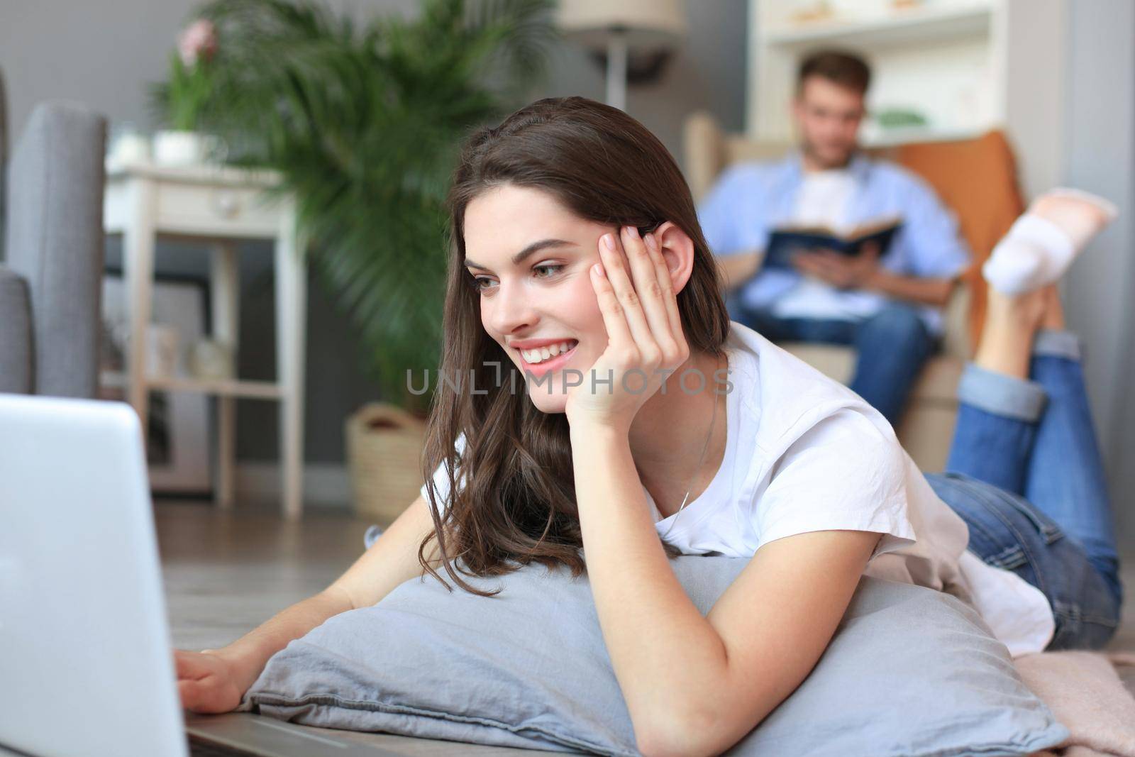 Smiling beautiful woman using laptop with blurred man in background at home. by tsyhun