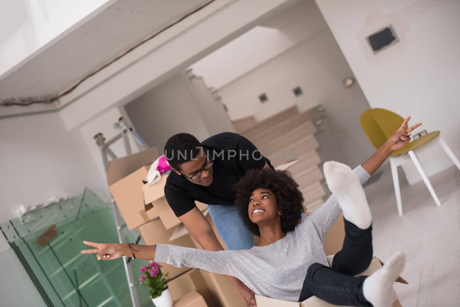 African American couple sitting in a box playing with packing material, having fun after moving in new home