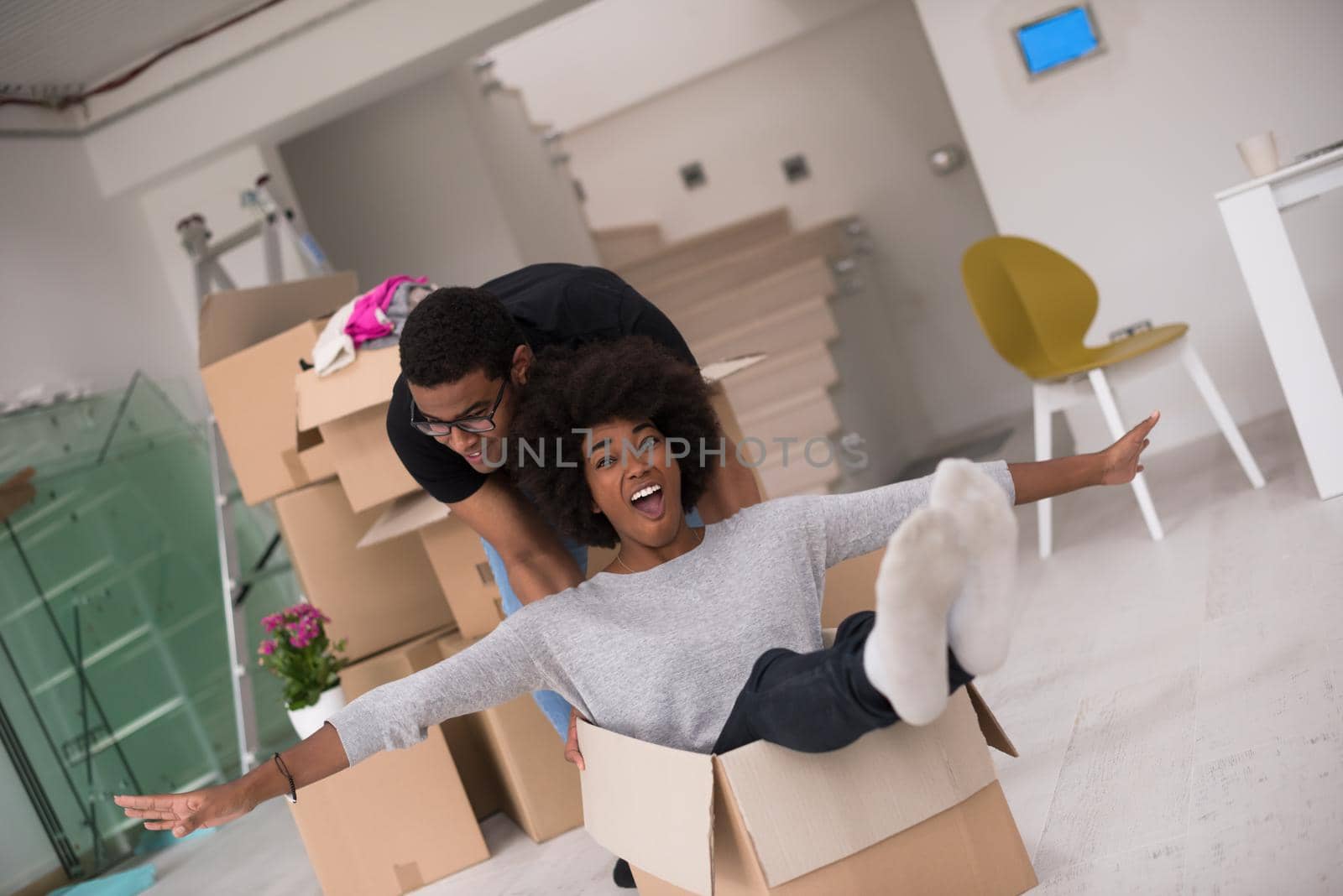 African American couple sitting in a box playing with packing material, having fun after moving in new home