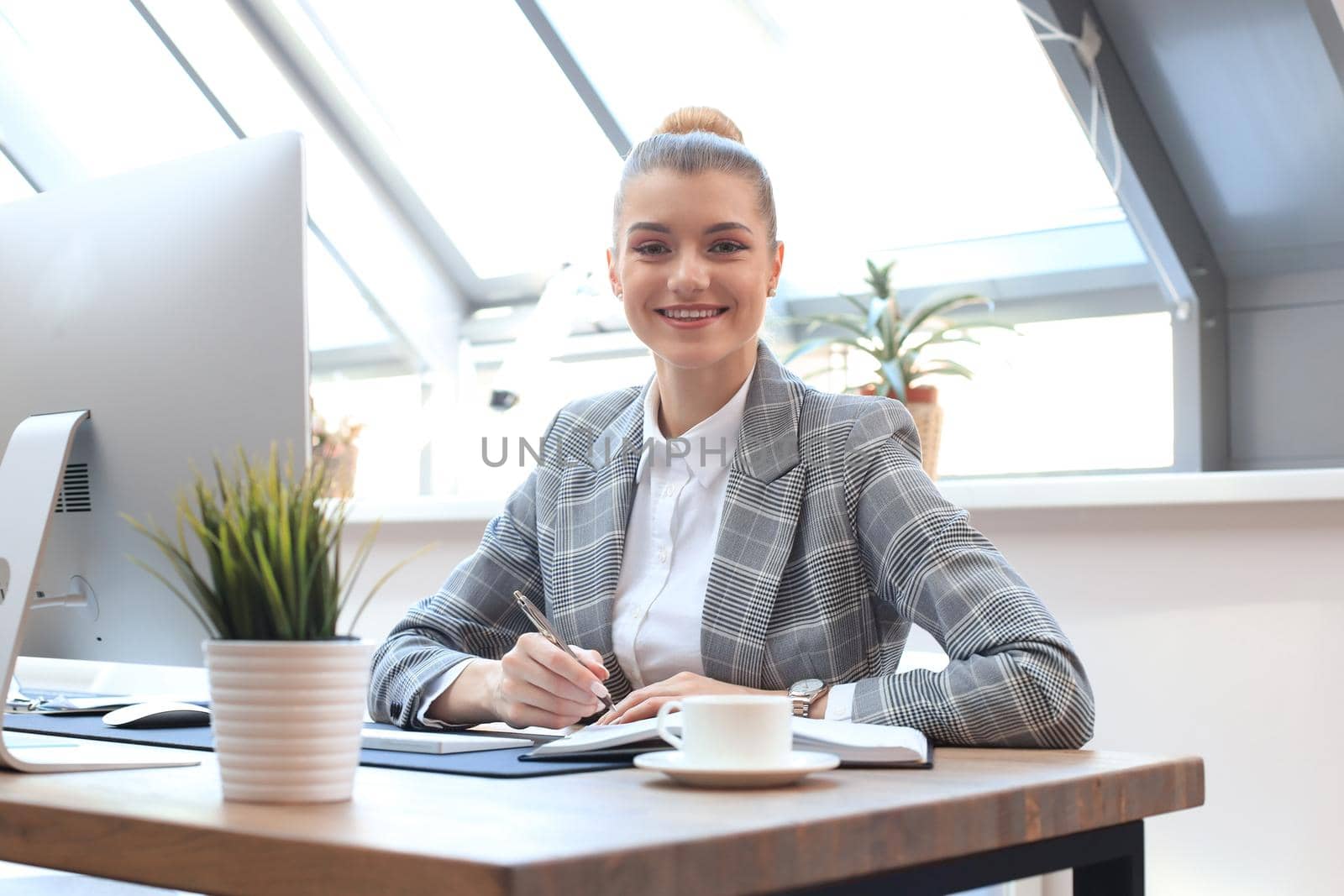 Portrait of a cheerful young businesswoman sitting at the table in office and looking at camera