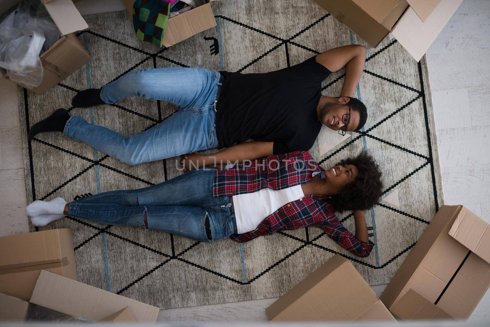 Top view of attractive young African American couple moving, holding hands, looking at camera and smiling while lying among cardboard boxes