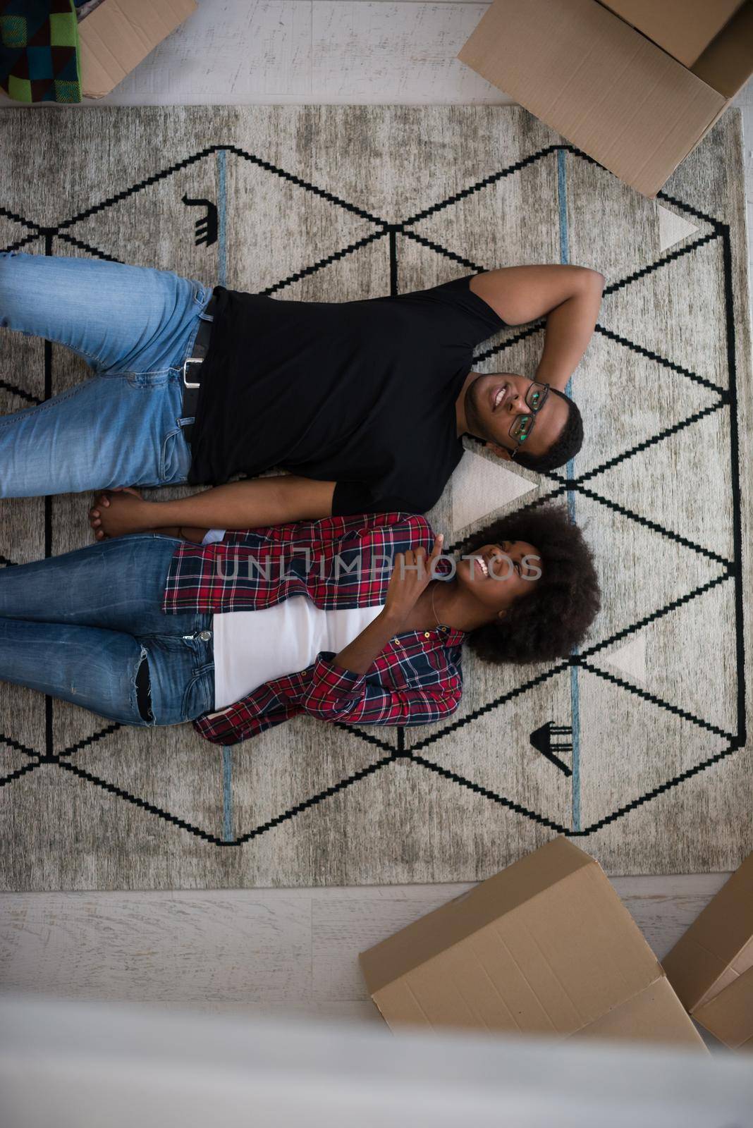 Top view of attractive young African American couple moving, holding hands, looking at camera and smiling while lying among cardboard boxes
