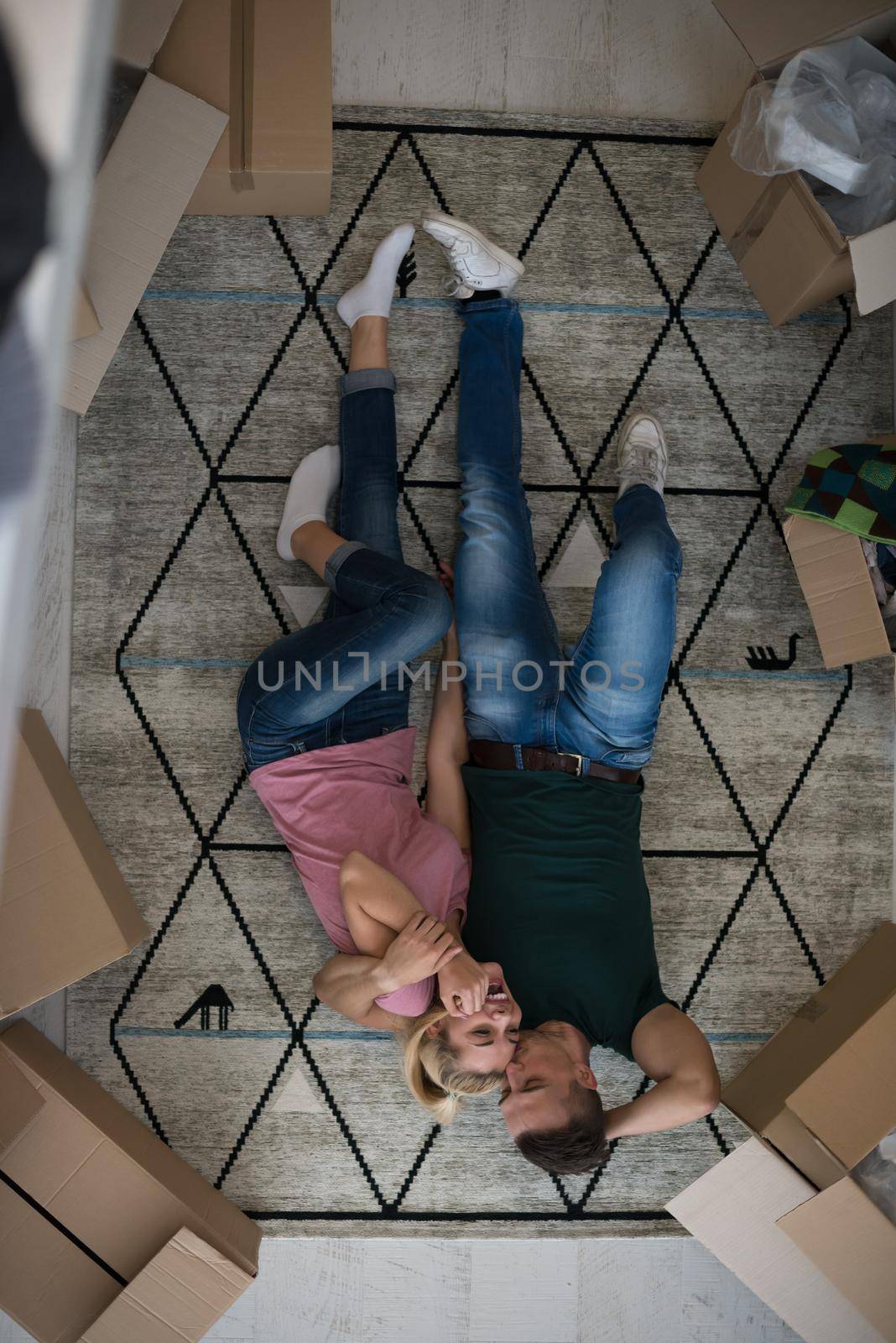 Top view of attractive young couple moving, holding hands, looking at camera and smiling while lying among cardboard boxes