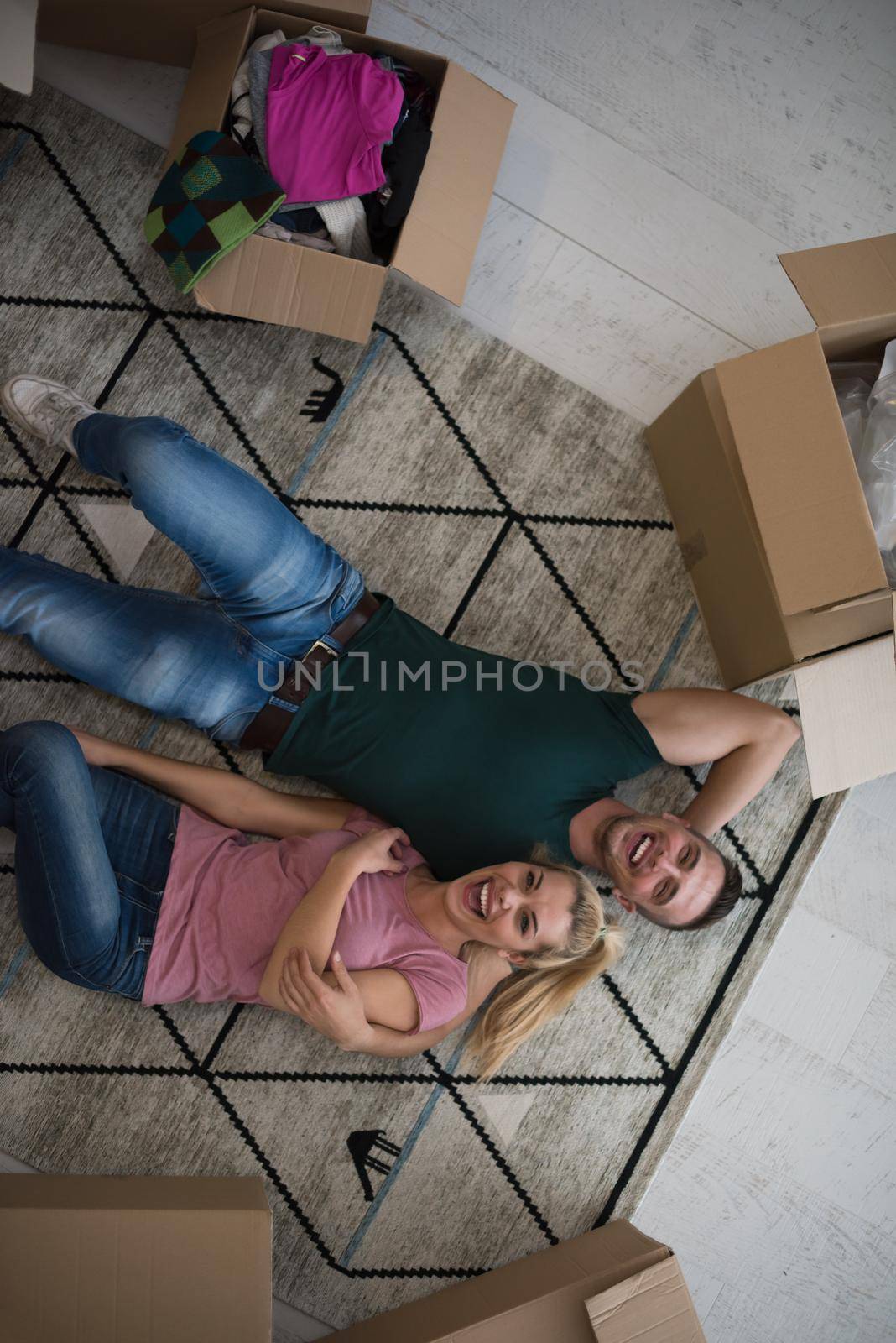 Top view of attractive young couple moving, holding hands, looking at camera and smiling while lying among cardboard boxes