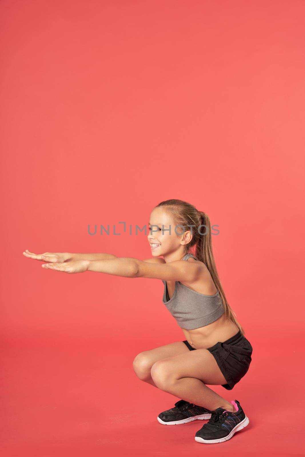 Adorable sporty girl looking away and smiling while doing exercise against red background