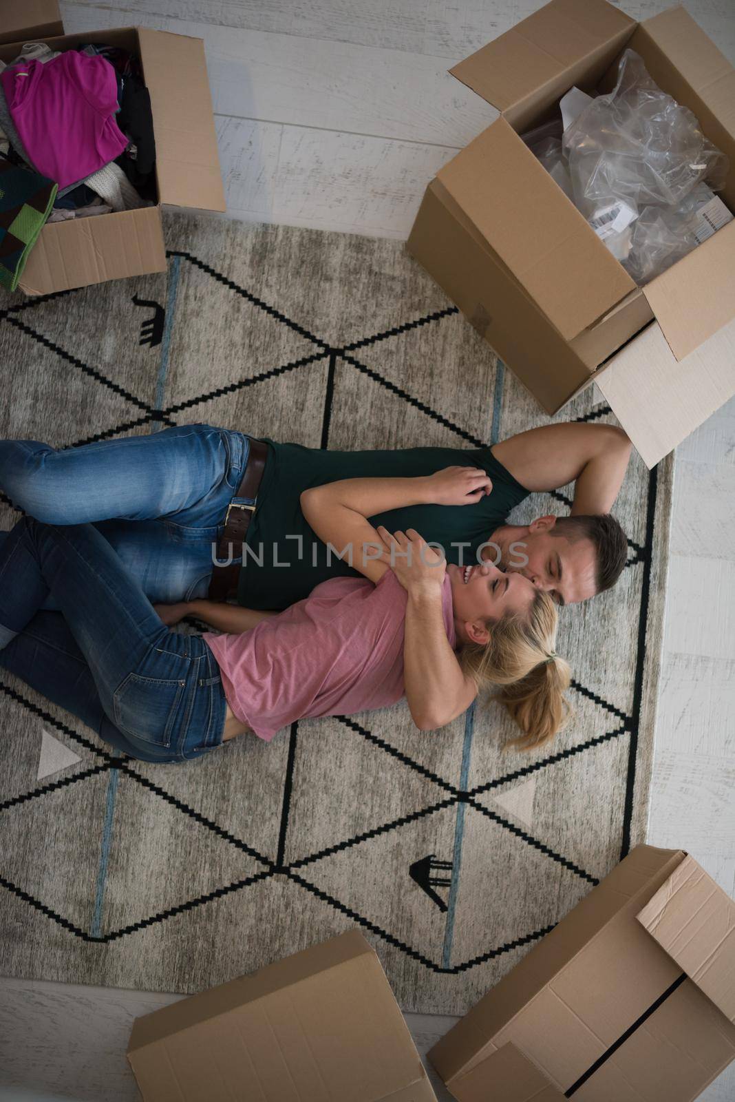 Top view of attractive young couple moving, holding hands, looking at camera and smiling while lying among cardboard boxes