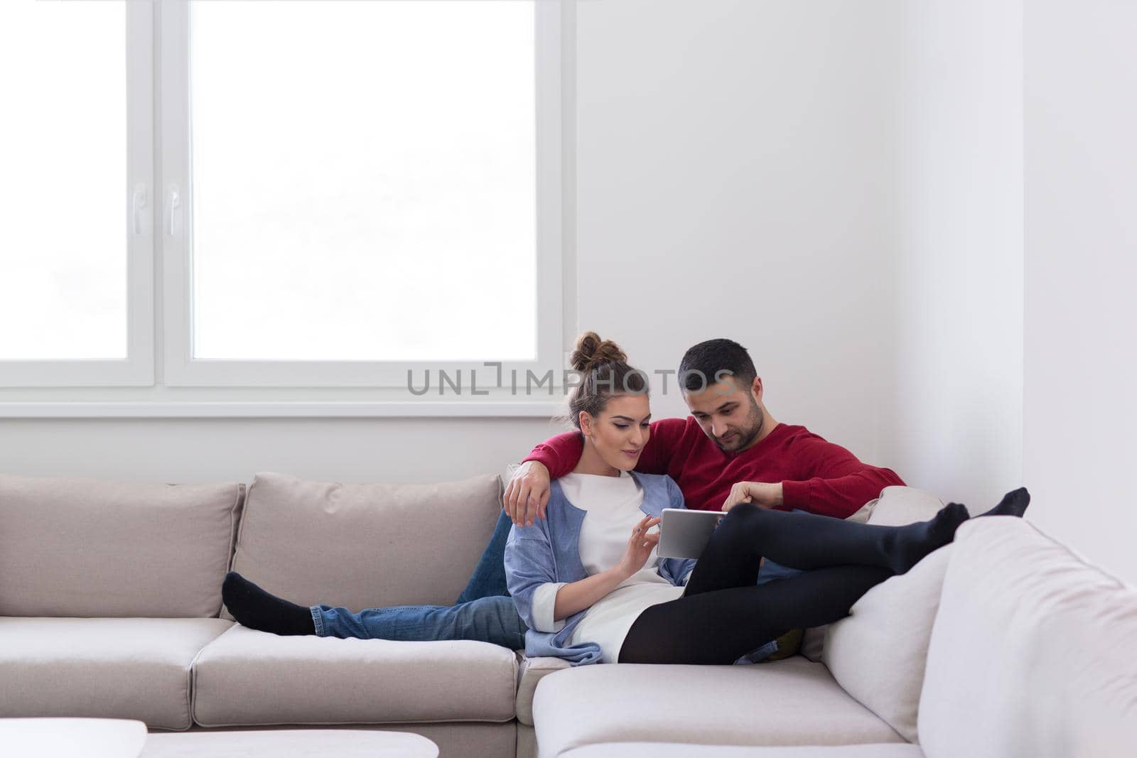 Young couple relaxing at  home using tablet computers reading in the living room on the sofa couch.