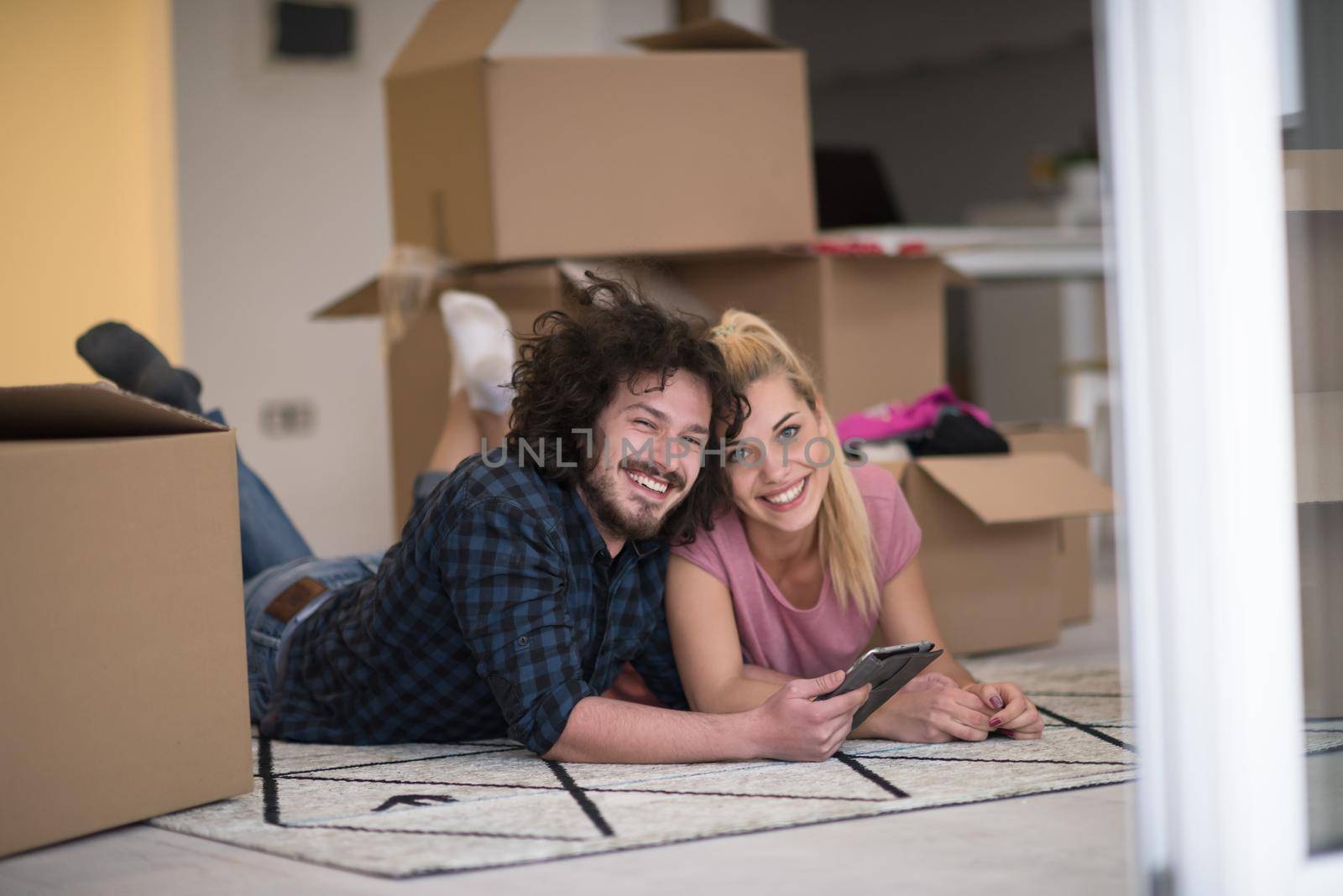 Young couple in love moving in a new flat, lying on the floor and surfing the web on a tablet computer in search of new redecoration ideas