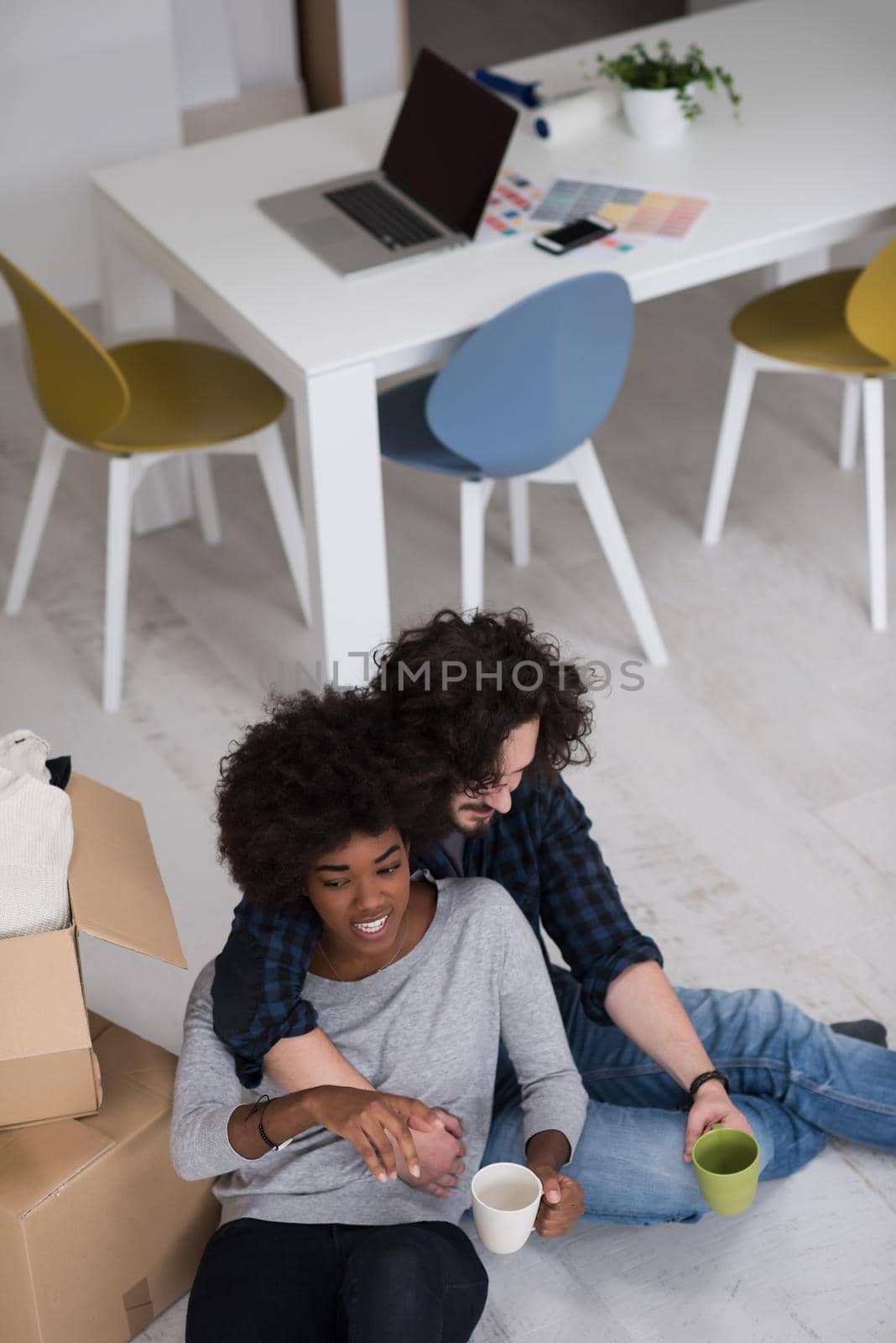 Relaxing in new house. Cheerful young multiethnic couple sitting on the floor and drinking coffee while cardboard boxes laying all around them