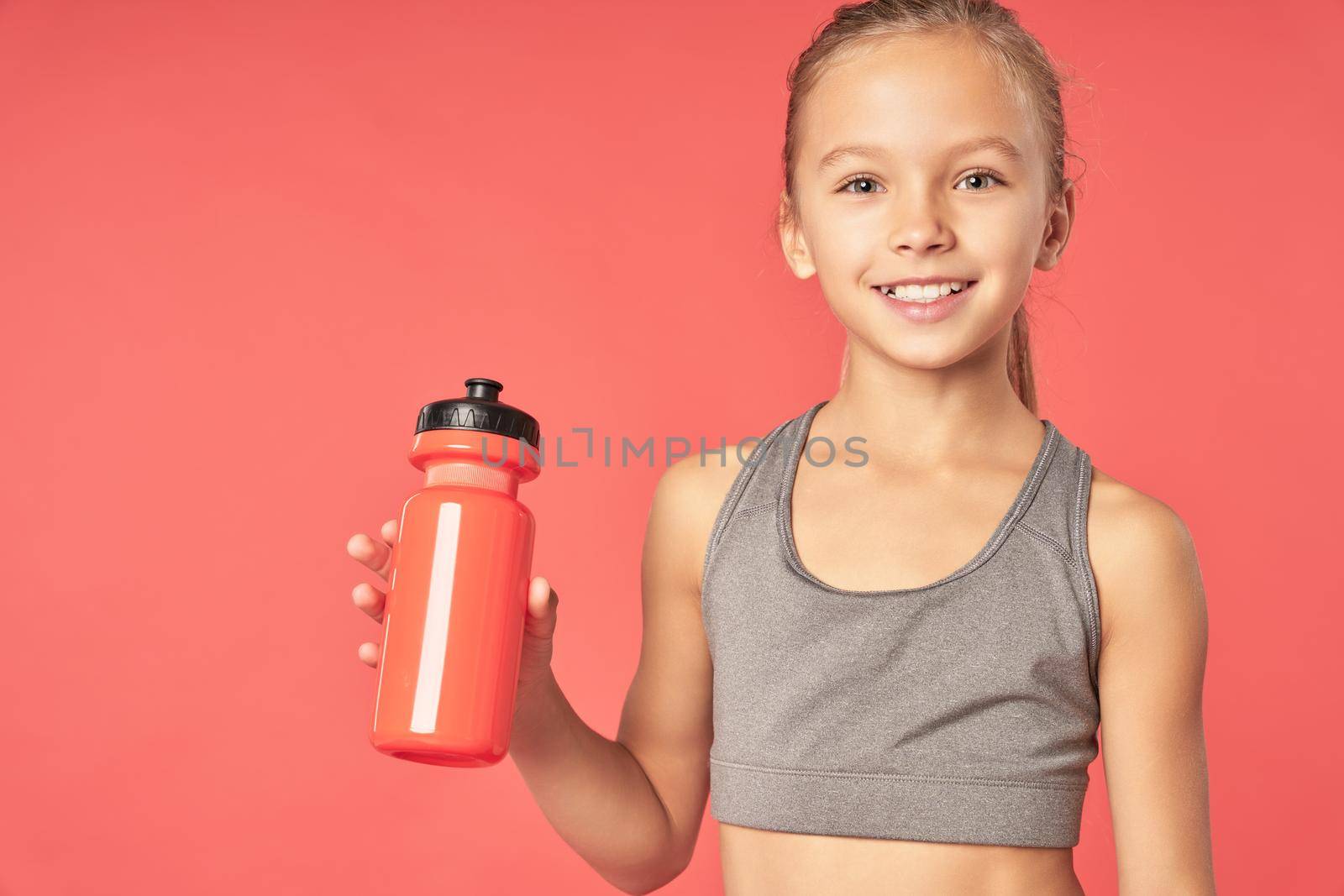 Cheerful female child with refreshing drink looking at camera and smiling while standing against red background