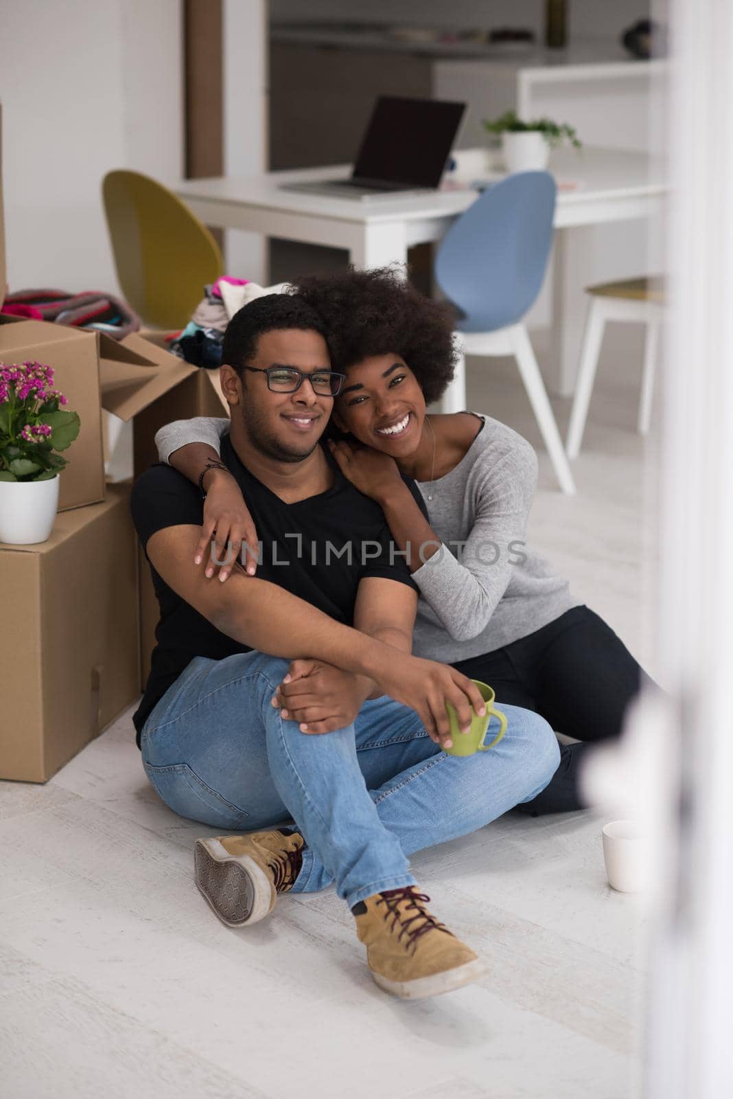 Relaxing in new house. Cheerful young African American couple sitting on the floor and drinking coffee while cardboard boxes laying all around them