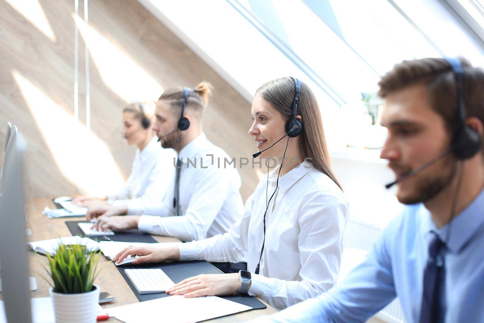 Female customer support operator with headset and smiling accompanied by her team