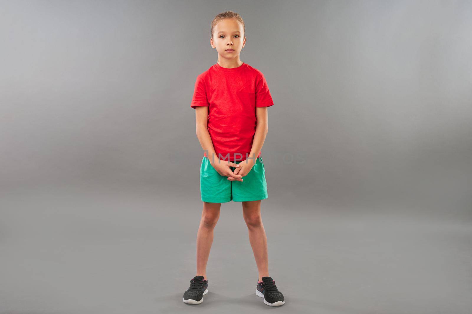Adorable girl in red shirt and sport shorts looking at camera with serious expression