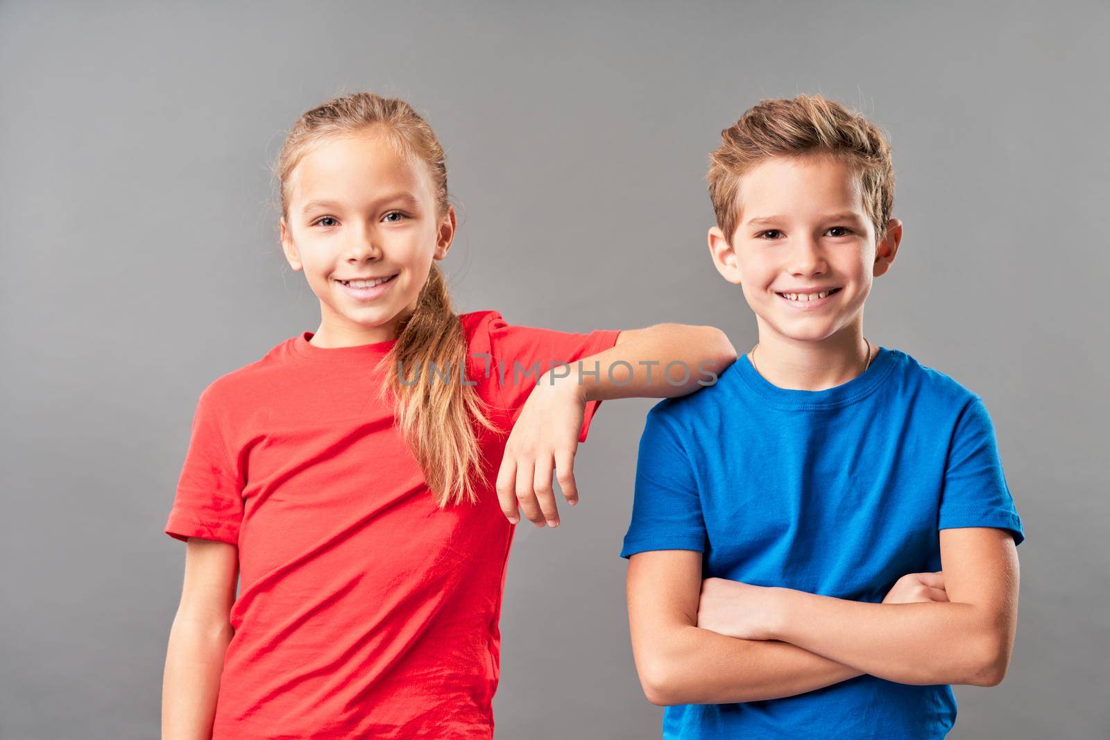 Cute female child placing hand on brother shoulder and smiling while boy crossing arms across his chest