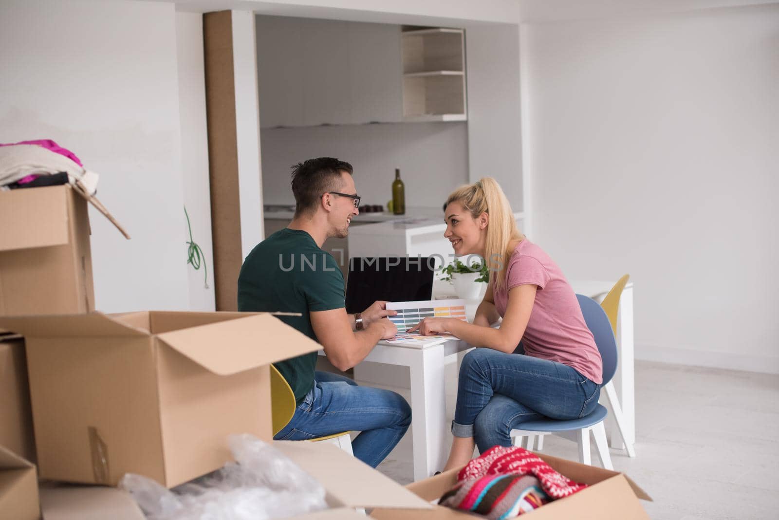 Young couple moving in a new home. Man and woman at the table using notebook laptop computer and plans with boxes around them