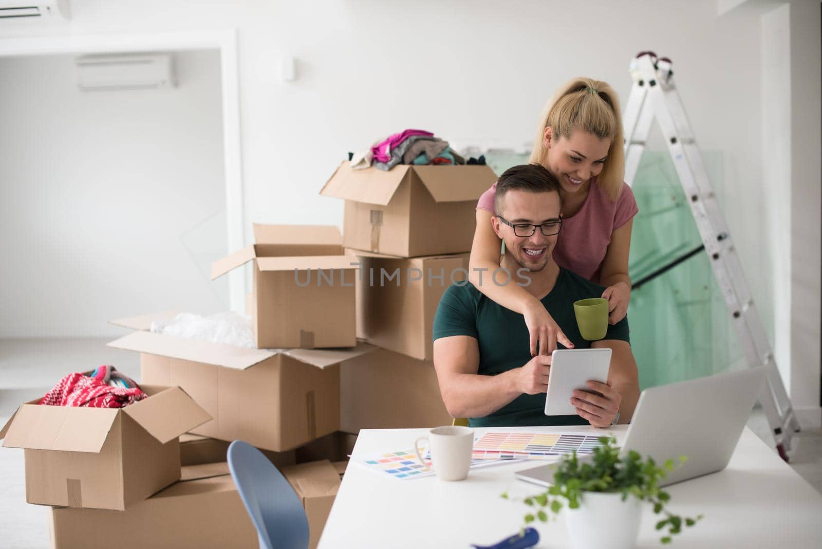 Young couple moving in a new home. Man and woman at the table using notebook laptop computer and plans with boxes around them