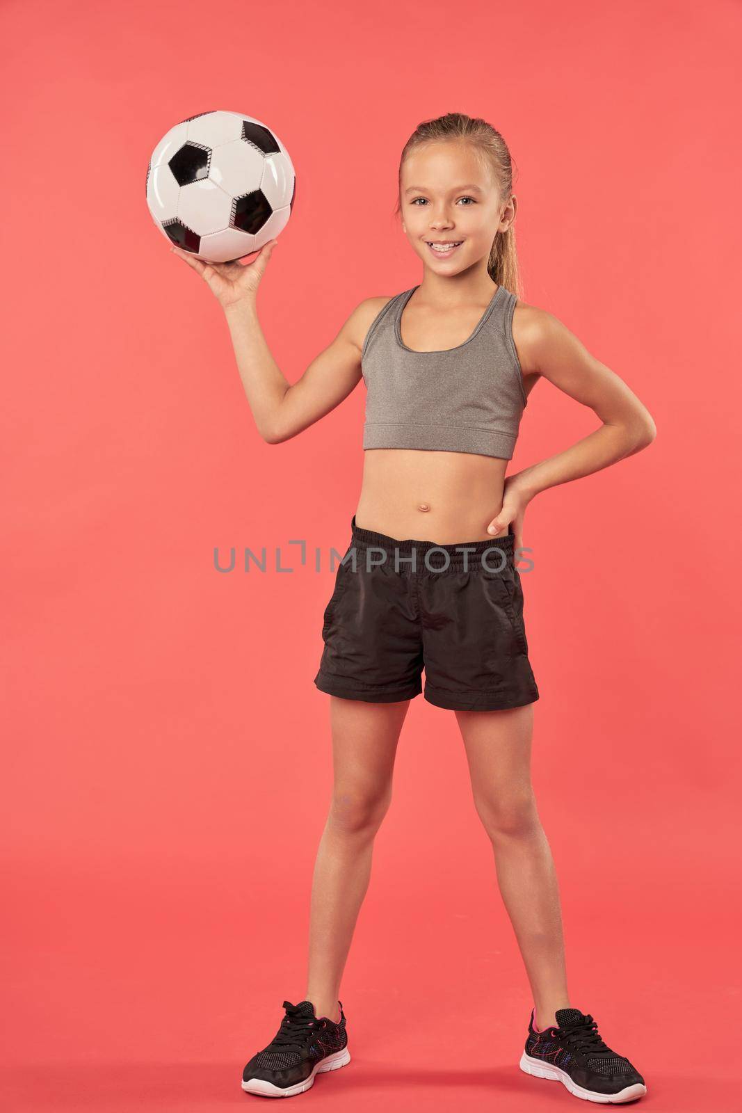Cute female child with soccer ball standing against red background by friendsstock