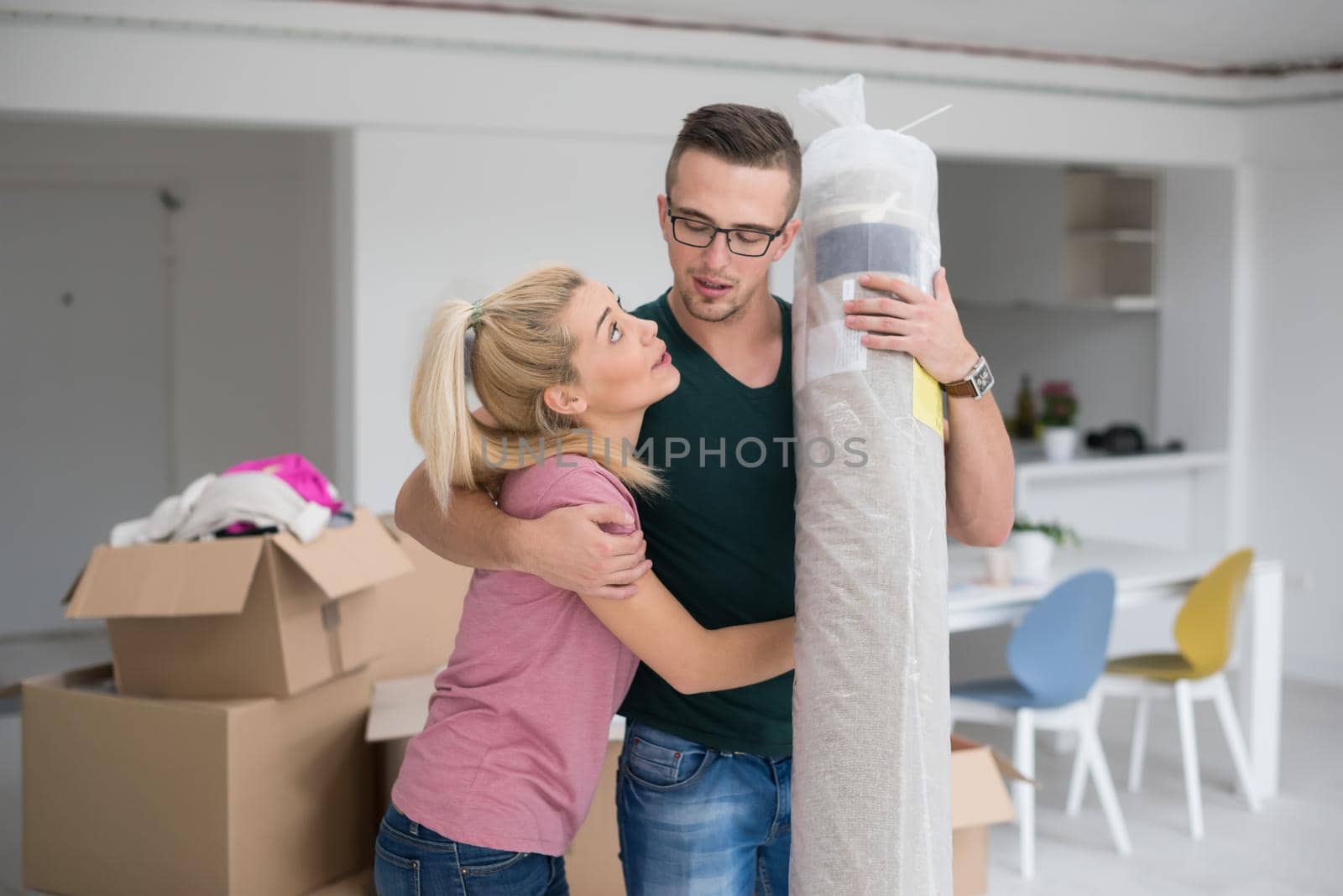 Young couple carrying a carpet moving in to new home together. Home, people, moving and real estate concept