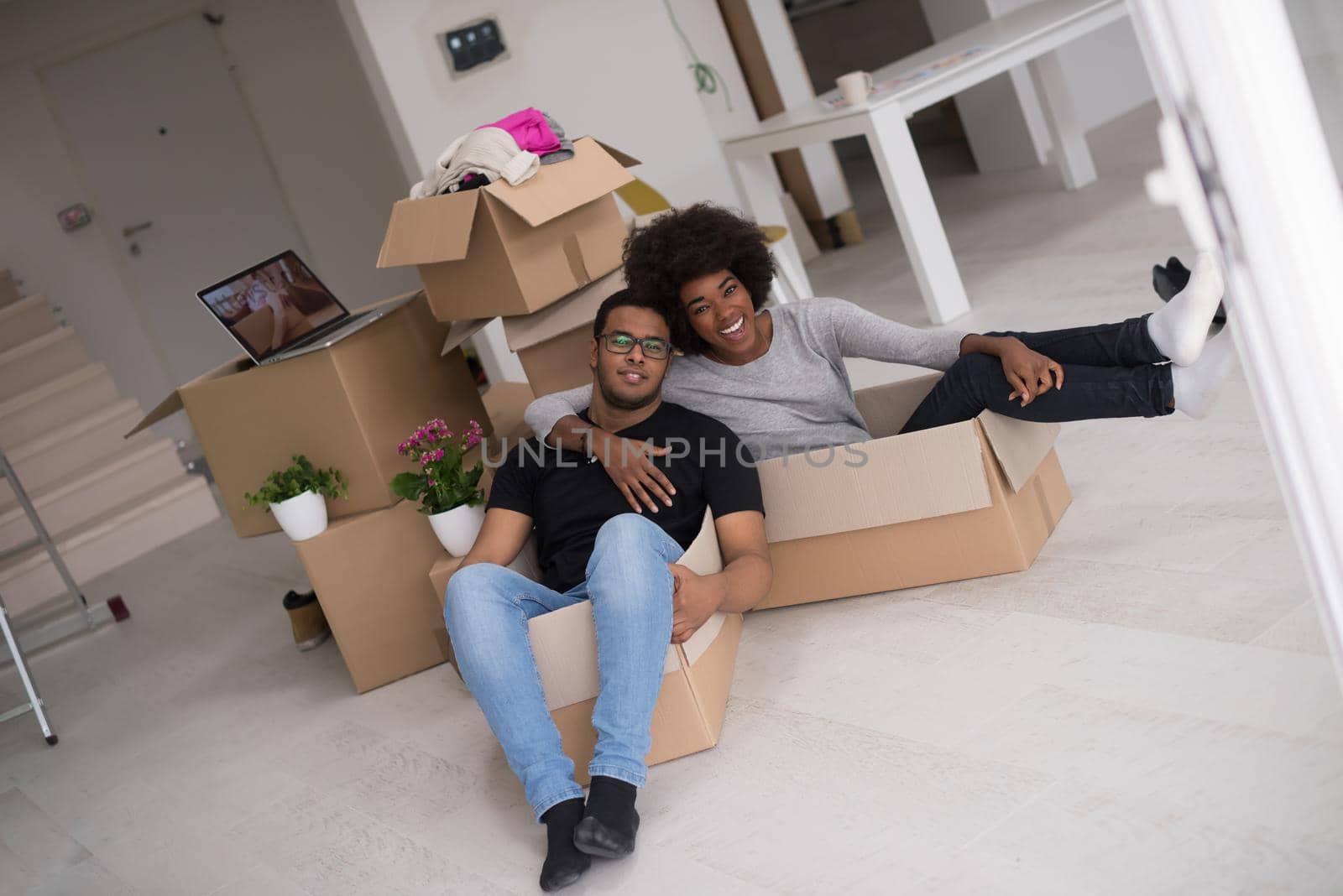 African American couple sitting in a box playing with packing material, having fun after moving in new home