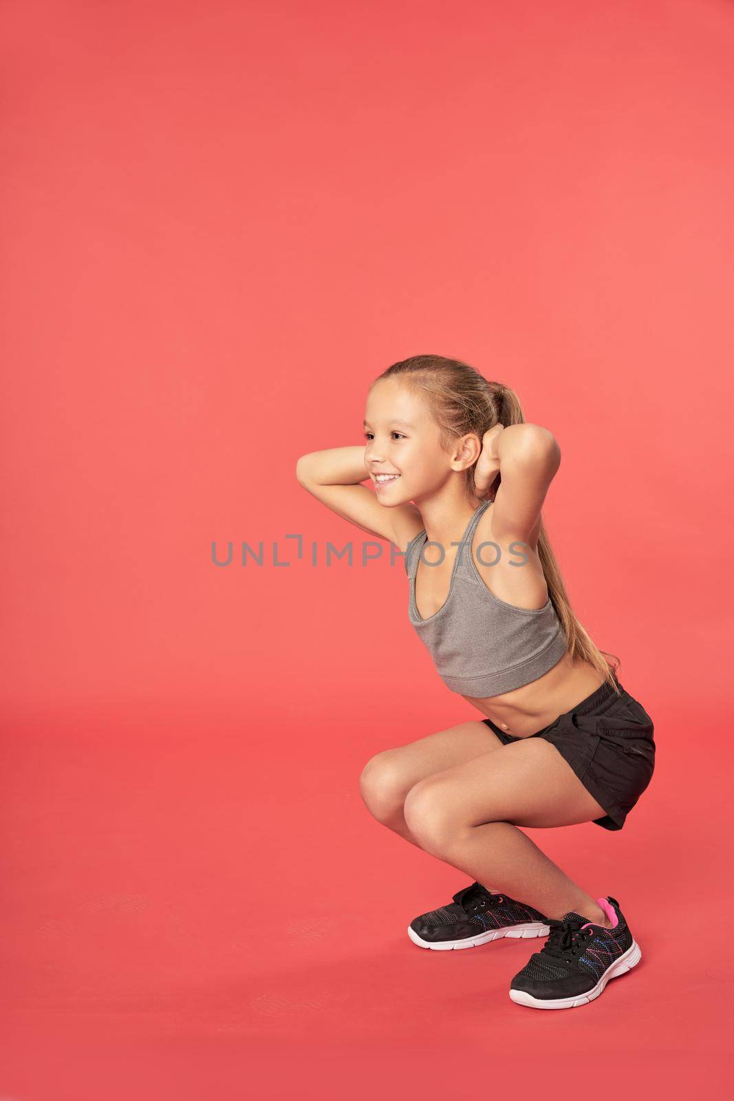 Cheerful sporty girl doing squats against red background by friendsstock