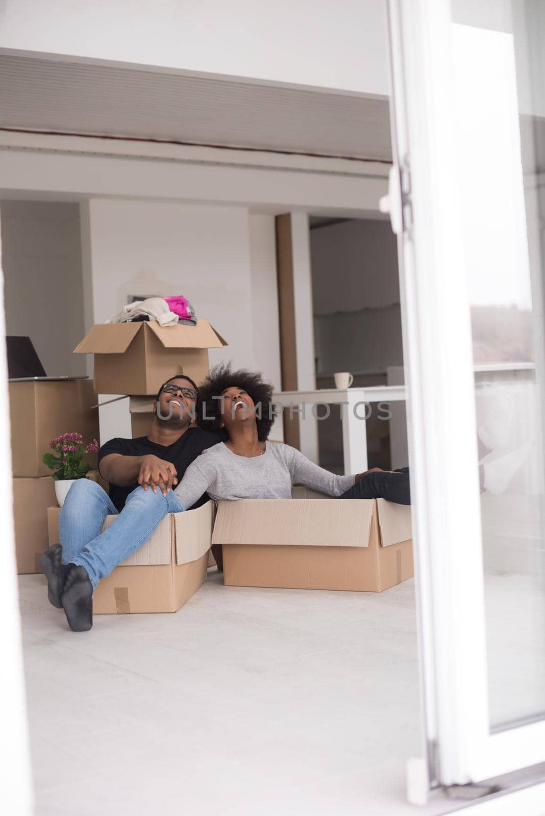 African American couple sitting in a box playing with packing material, having fun after moving in new home