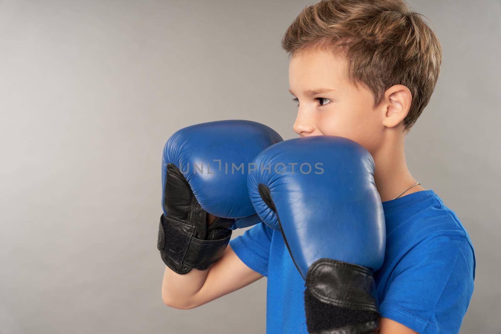 Adorable boy boxer wearing sports boxing gloves and blue shirt while doing fighting stance