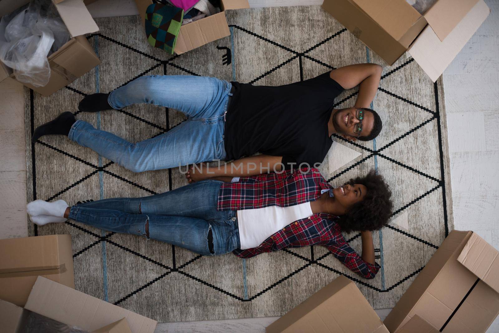 Top view of attractive young African American couple moving, holding hands, looking at camera and smiling while lying among cardboard boxes