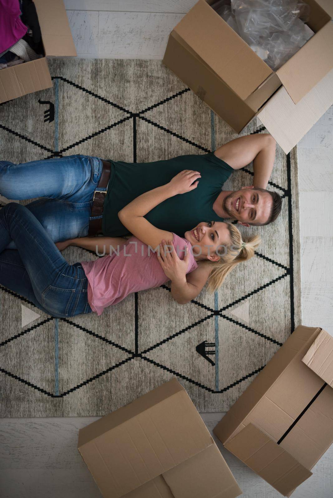 Top view of attractive young couple moving, holding hands, looking at camera and smiling while lying among cardboard boxes