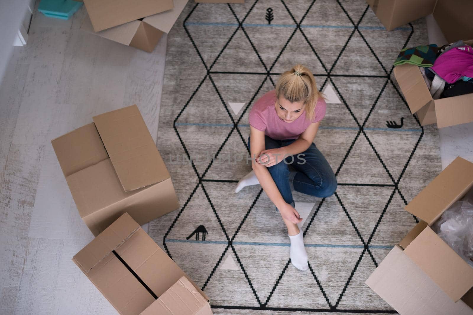 top view of young beautiful woman sitting and relaxing on the floor after moving into a new home with cardboard boxes around her