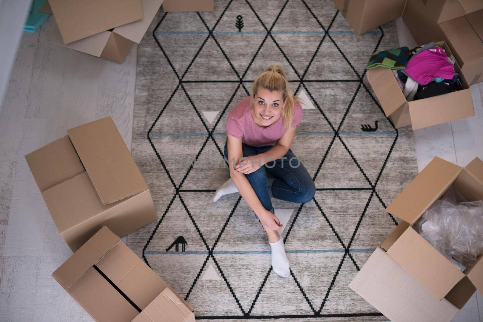 top view of young beautiful woman sitting and relaxing on the floor after moving into a new home with cardboard boxes around her