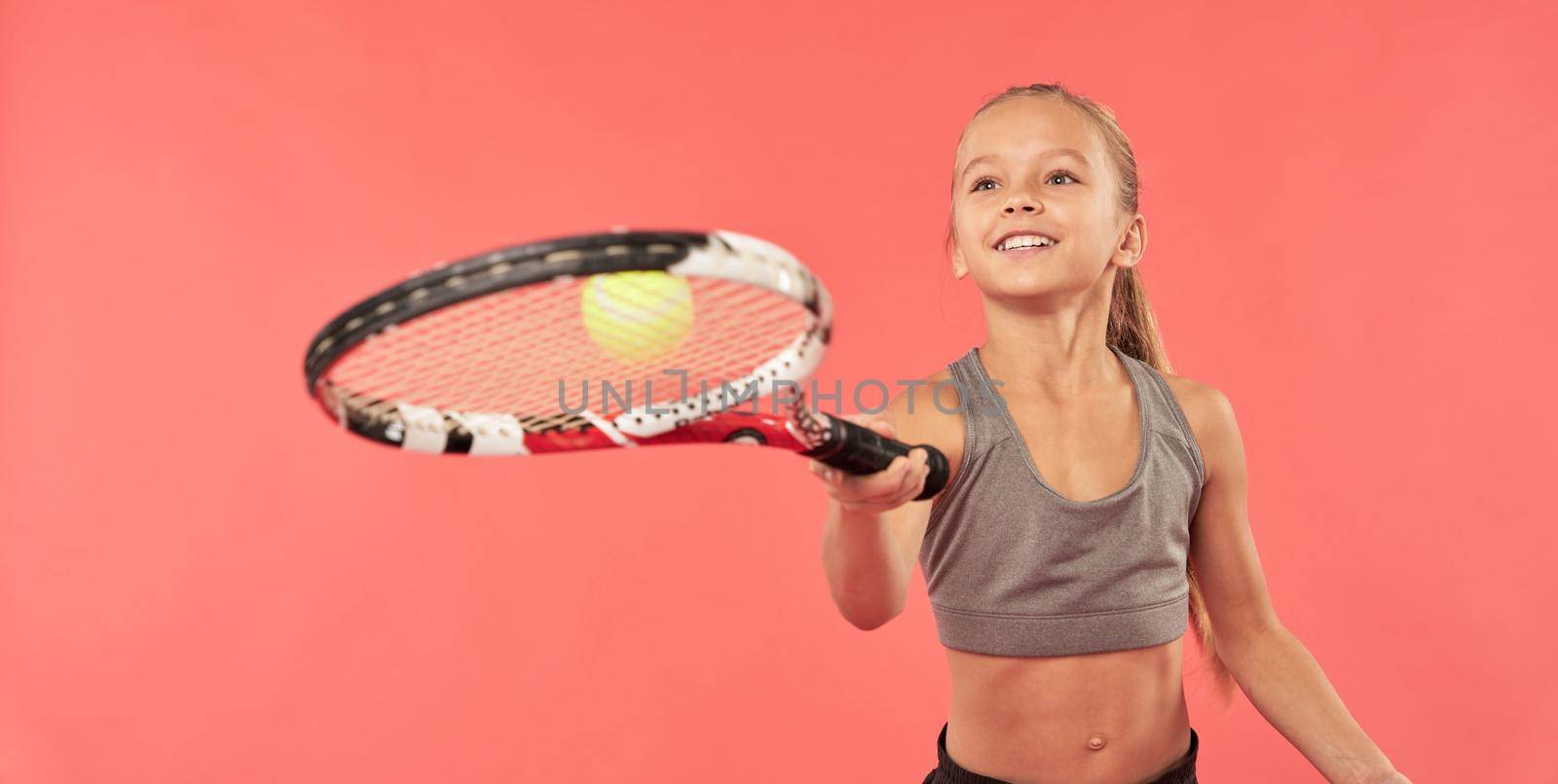 Adorable girl tennis player wearing sports crop top while bouncing tennis ball on racket and smiling