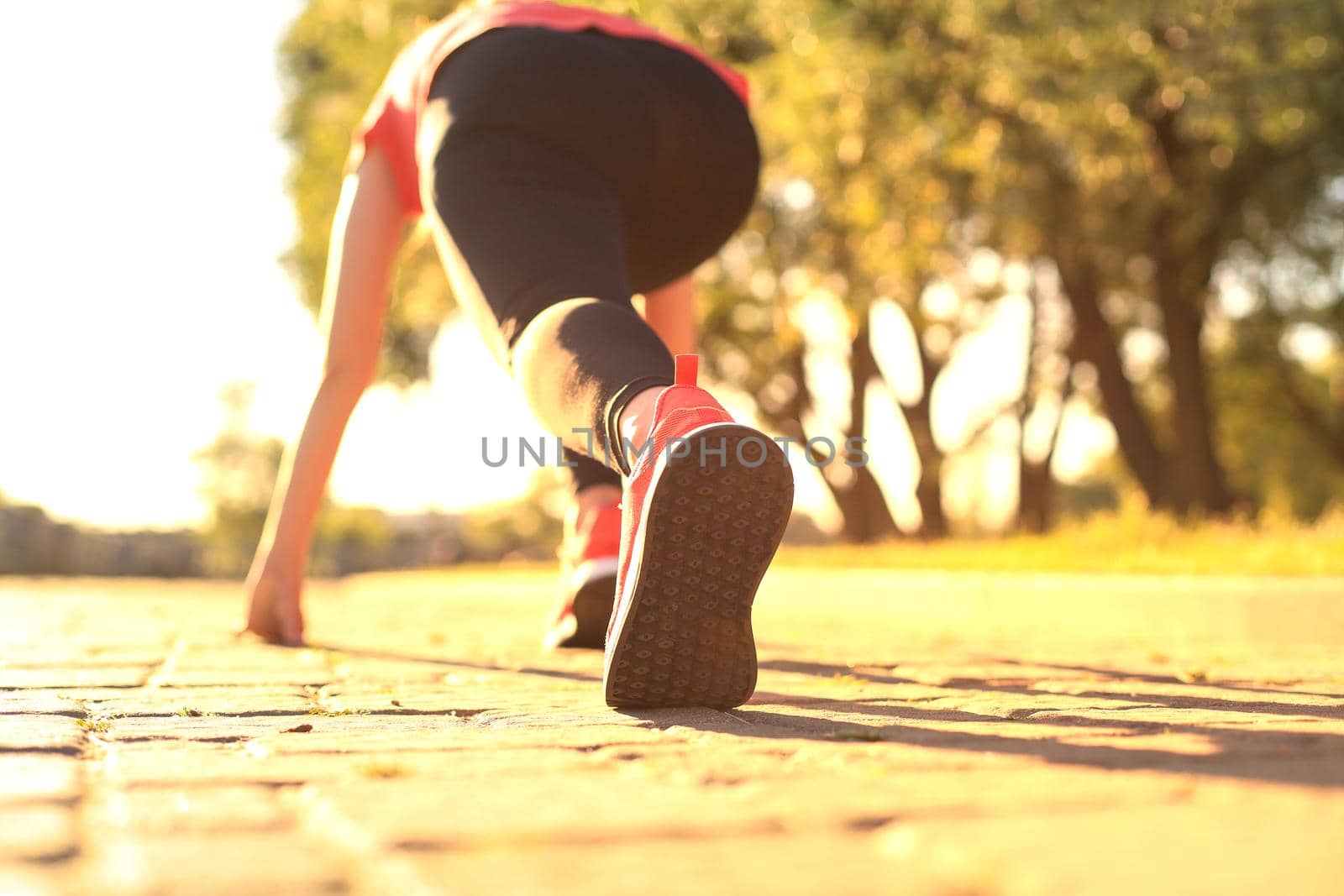 Top rear view of young woman in sports clothing standing on the start line while running outdoors. by tsyhun