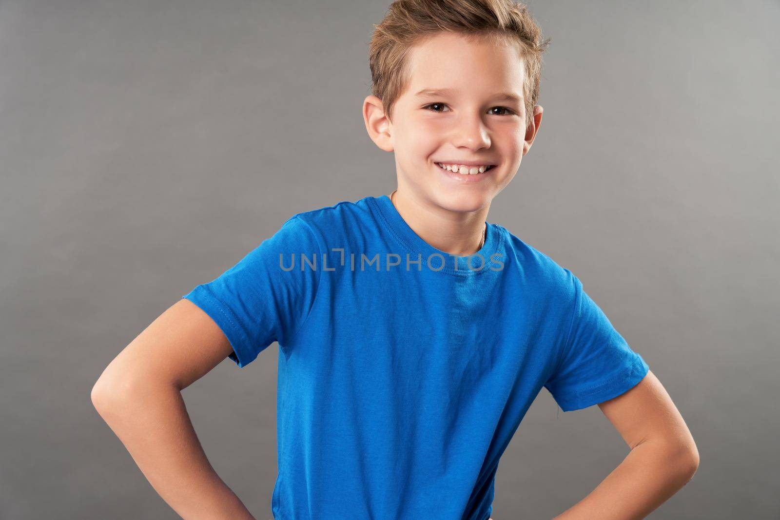 Cute cheerful boy standing against gray background by friendsstock