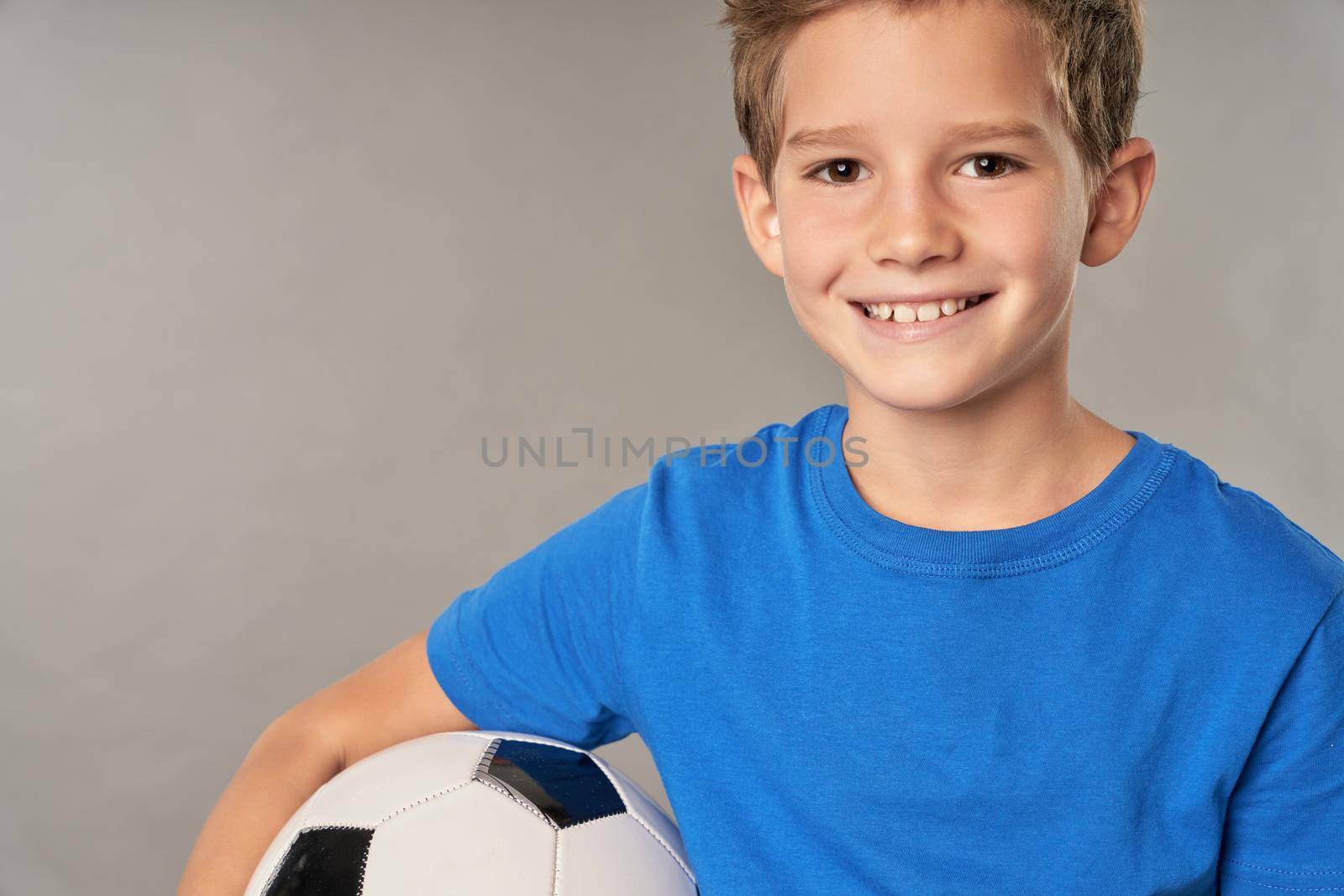 Close up of adorable male child football player looking at camera and smiling while holding soccer ball