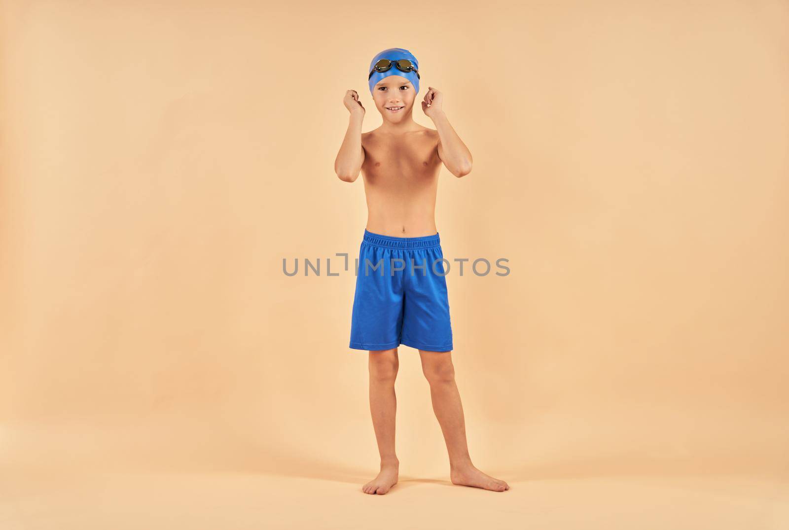 Adorable male child wearing swim trunks and cap while looking away and smiling