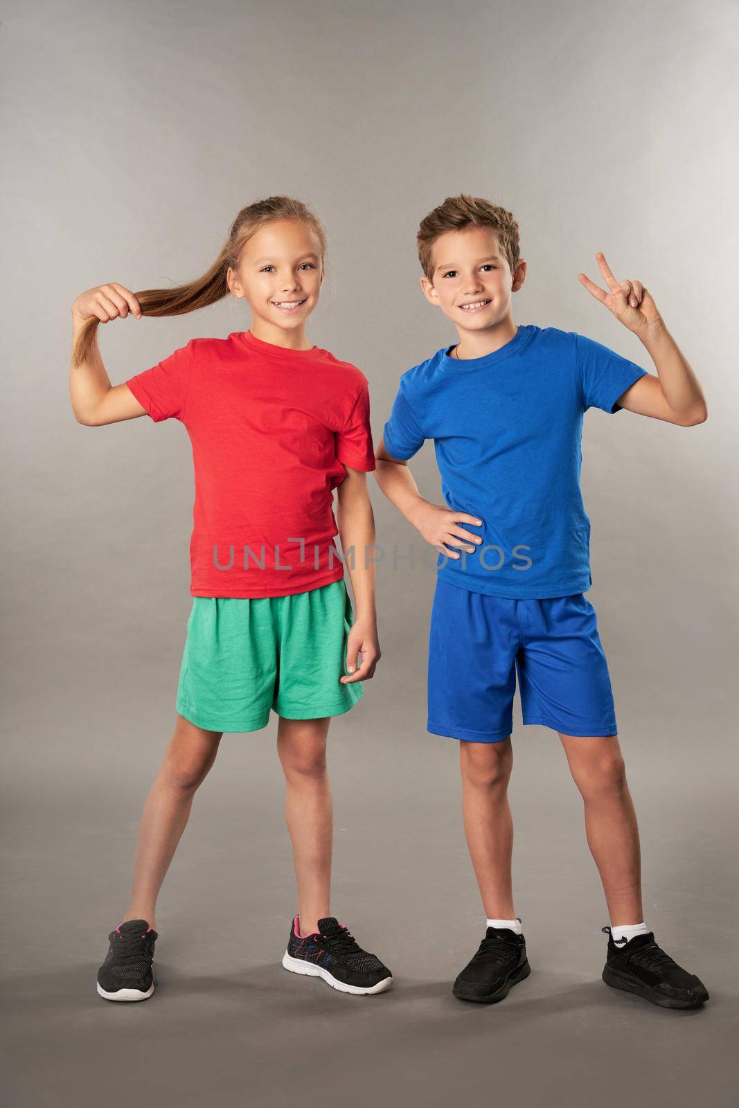 Cute female child in shorts looking at camera and smiling while male kid showing victory gesture