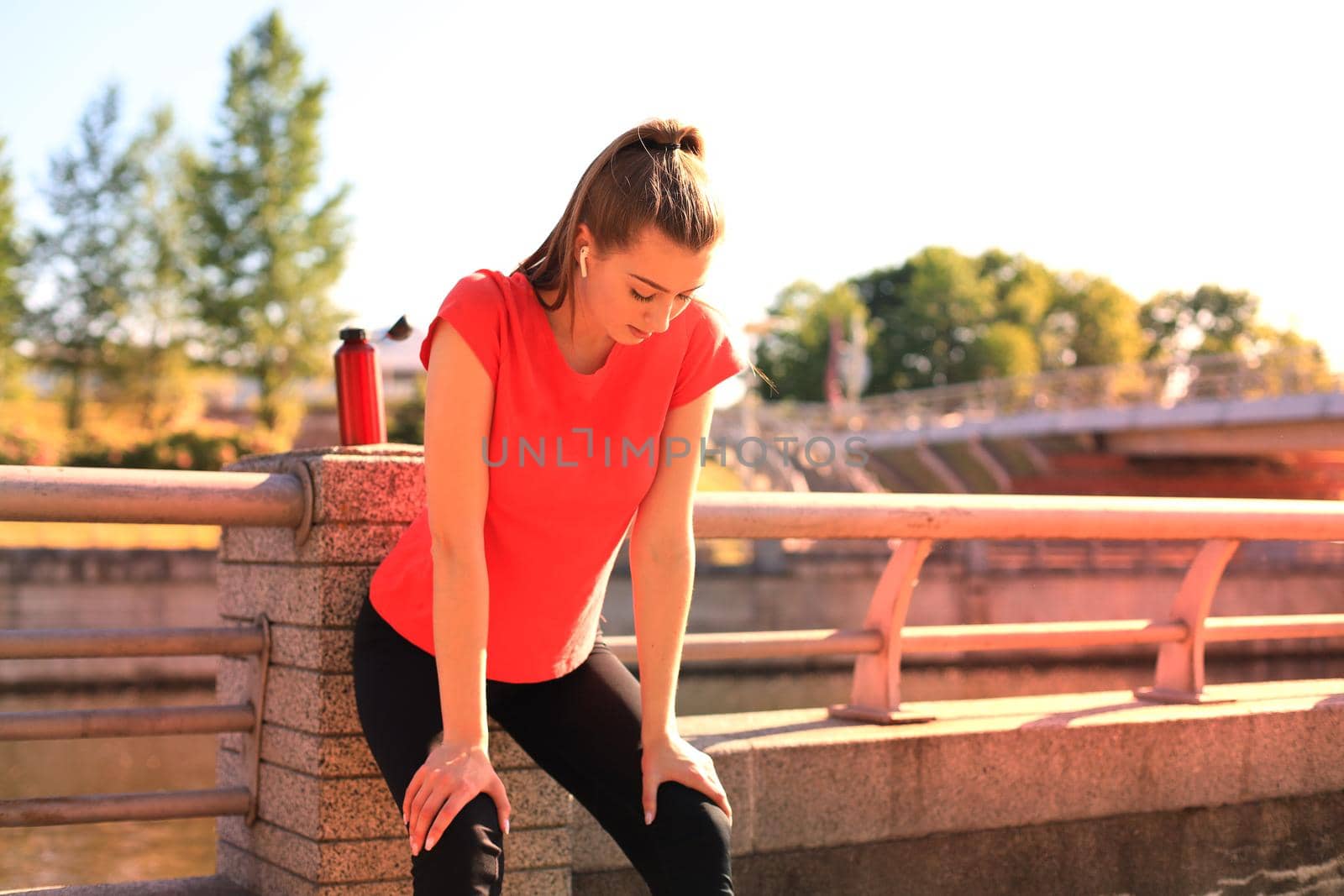 Attractive young woman in sports clothing taking a break while sitting outdoors. by tsyhun