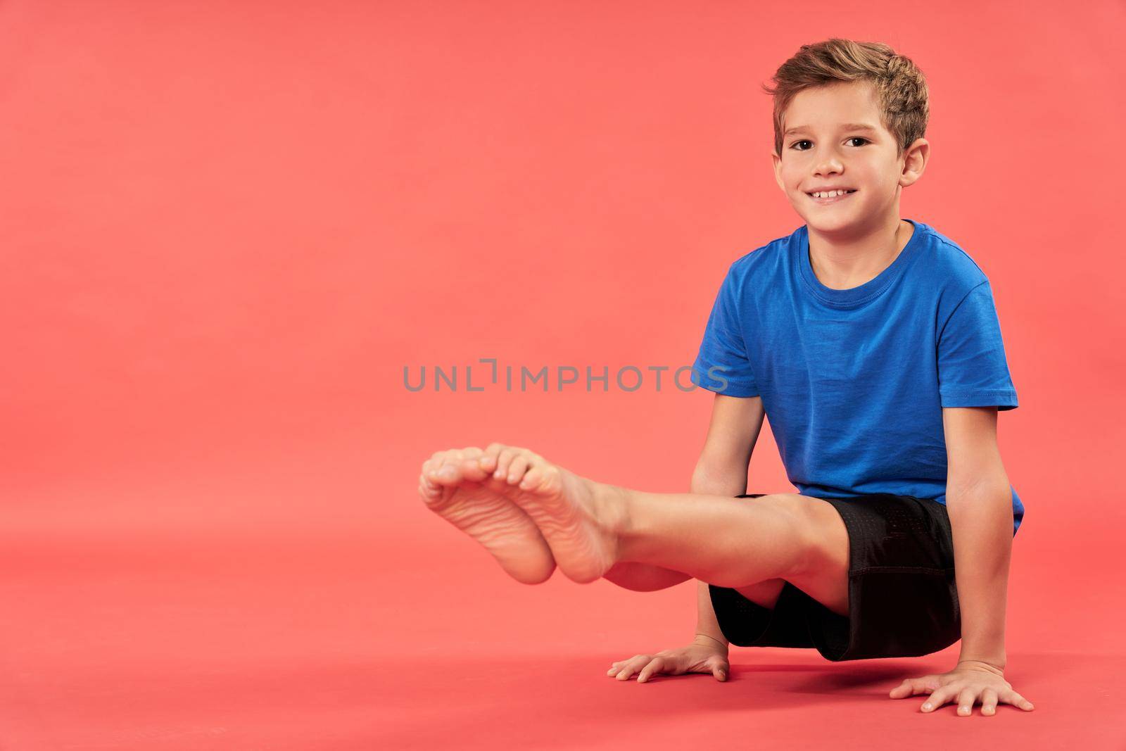 Adorable male child in sportswear looking at camera and smiling while lifting himself up and balancing on two hands