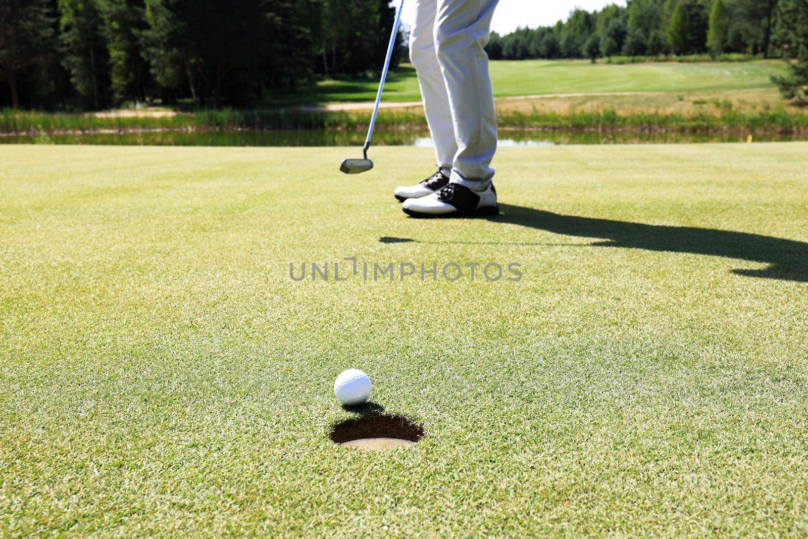 Golf player at the putting green hitting ball into a hole